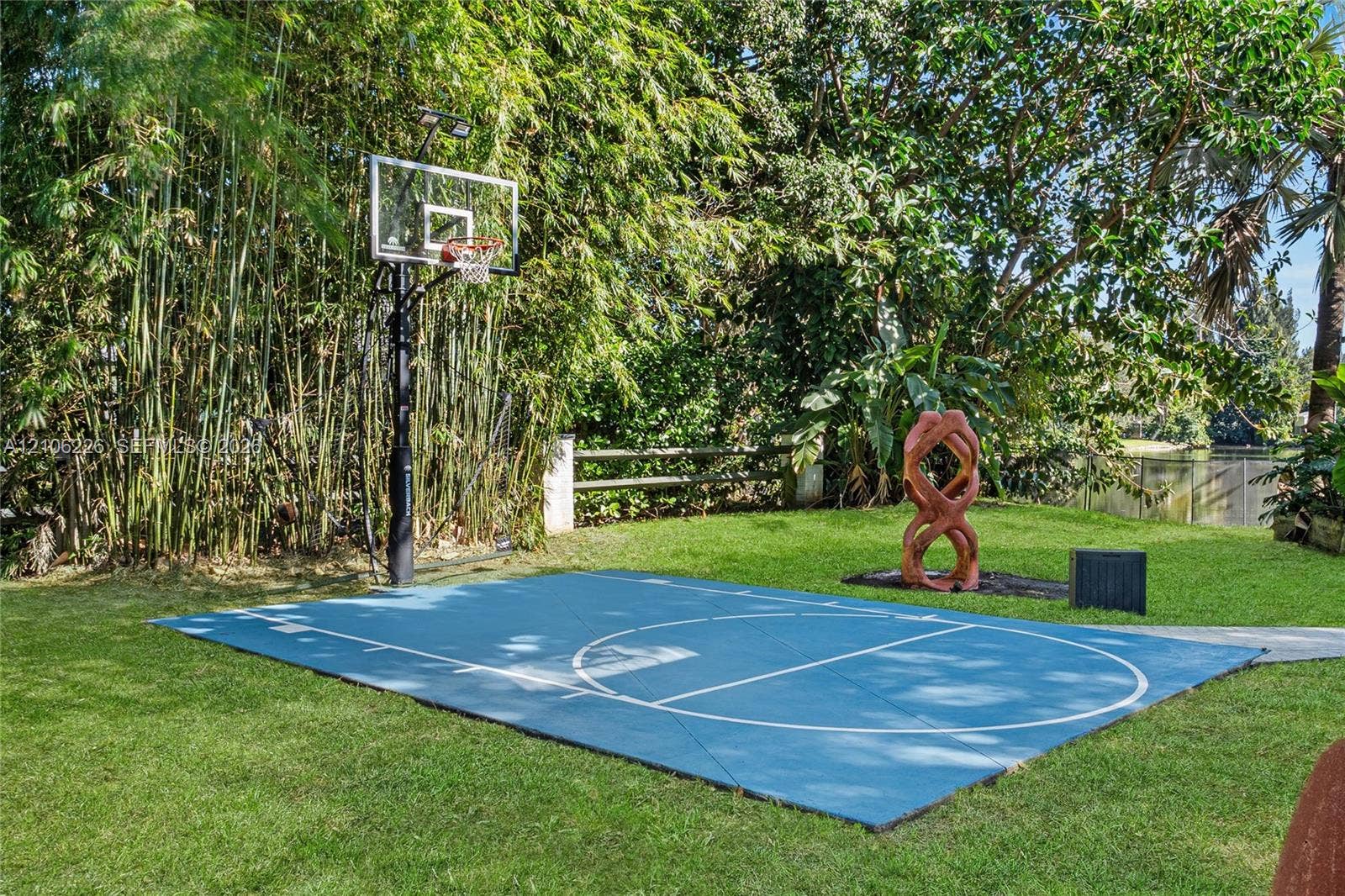 11155 SW 40th Street, Davie, FL 33328 Backyard sports court featuring a blue surface with white court markings and an attached basketball hoop, surrounded by mature trees and landscaped vegetation