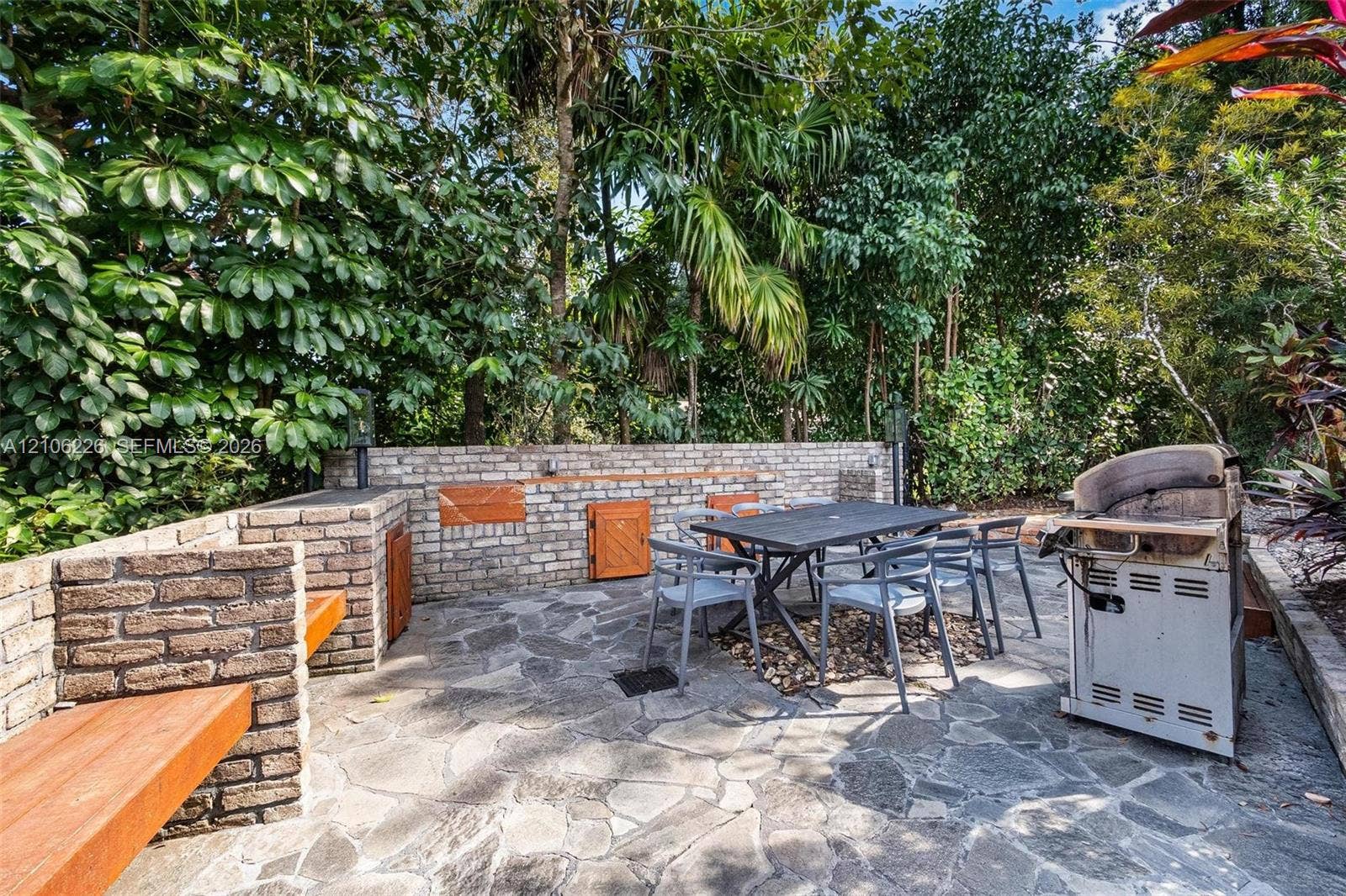 11155 SW 40th Street, Davie, FL 33328 Outdoor patio featuring irregular flagstone paving, integrated brick masonry walls, built-in wood-finish bench seating, and wood-panel cabinet access doors