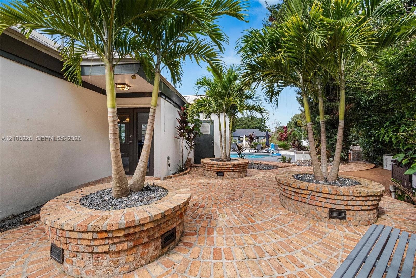 11155 SW 40th Street, Davie, FL 33328 Exterior patio featuring a circular brick paver pattern, custom tiered brick planters, and mature palm trees