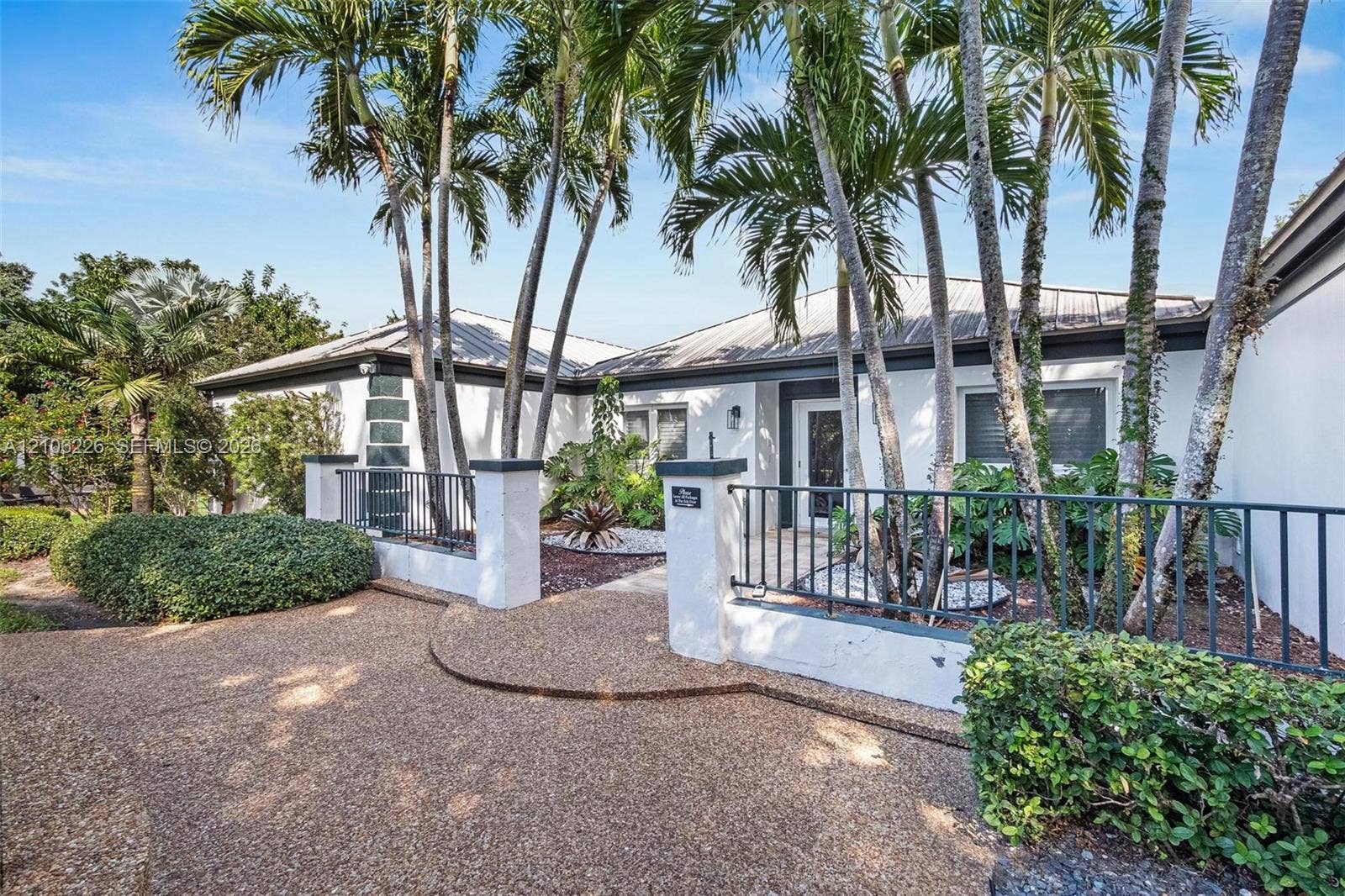 11155 SW 40th Street, Davie, FL 33328 Exterior facade featuring stucco siding, metal roof, paved walkway, metal perimeter fencing, and mature palm trees