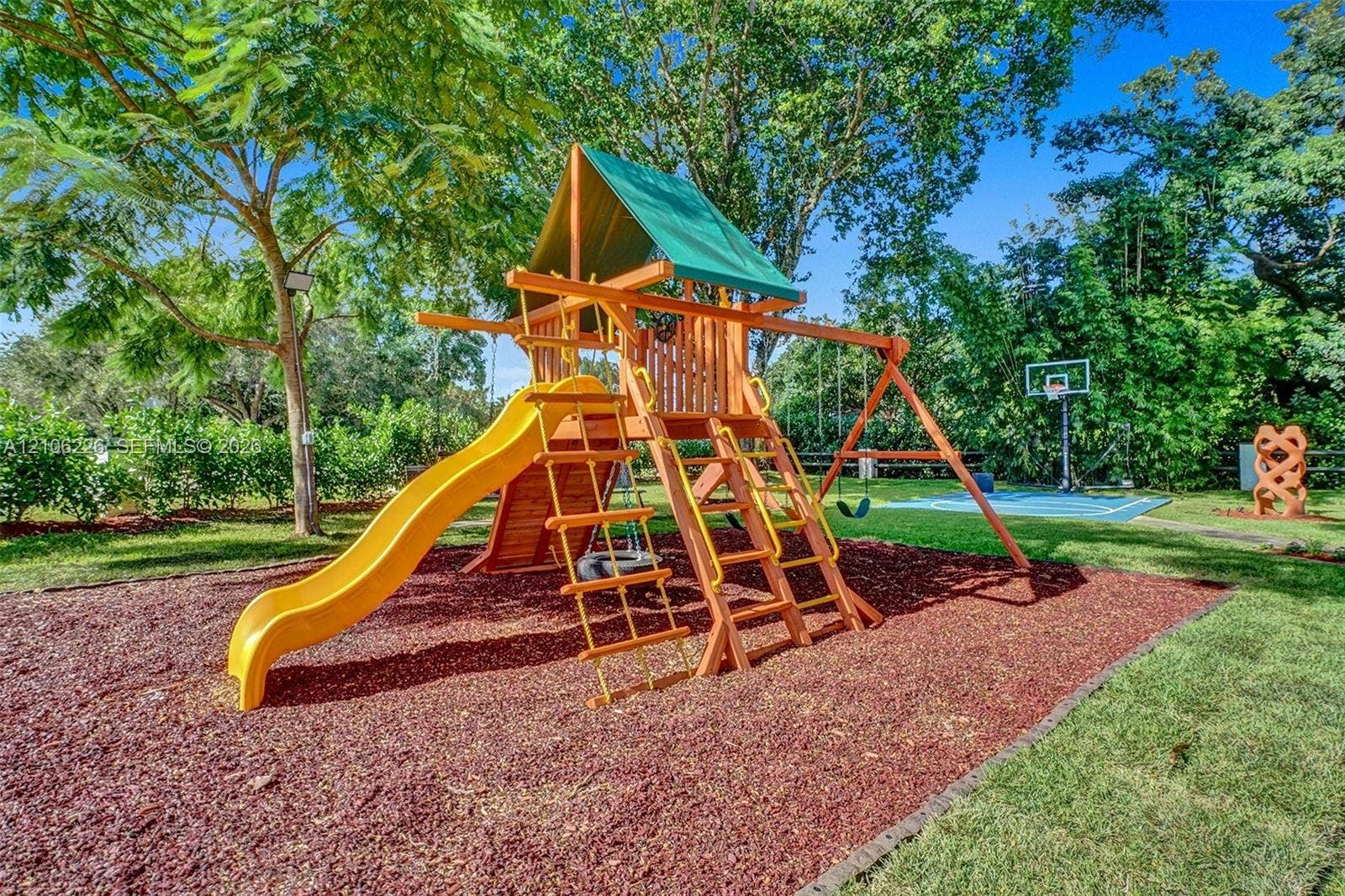 11155 SW 40th Street, Davie, FL 33328 Backyard recreation area featuring a multi-component wooden playset, wood-chip ground cover, and a paved basketball court with a hoop