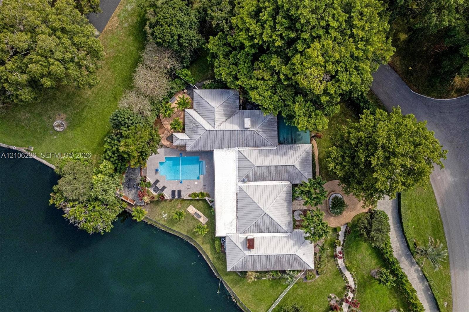 11155 SW 40th Street, Davie, FL 33328 Aerial perspective featuring a waterfront property with a metal roof, an in-ground swimming pool, stone-paver hardscaping, and mature trees