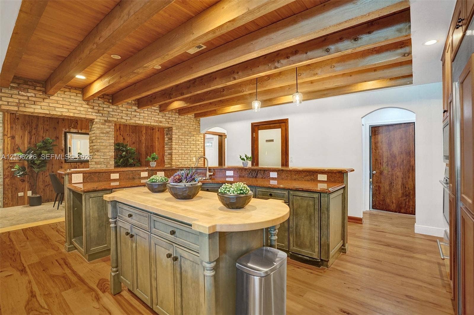 11155 SW 40th Street, Davie, FL 33328 Kitchen featuring exposed wood ceiling beams, brick wall accents, custom cabinetry, a wood-topped center island, and wood-finish flooring