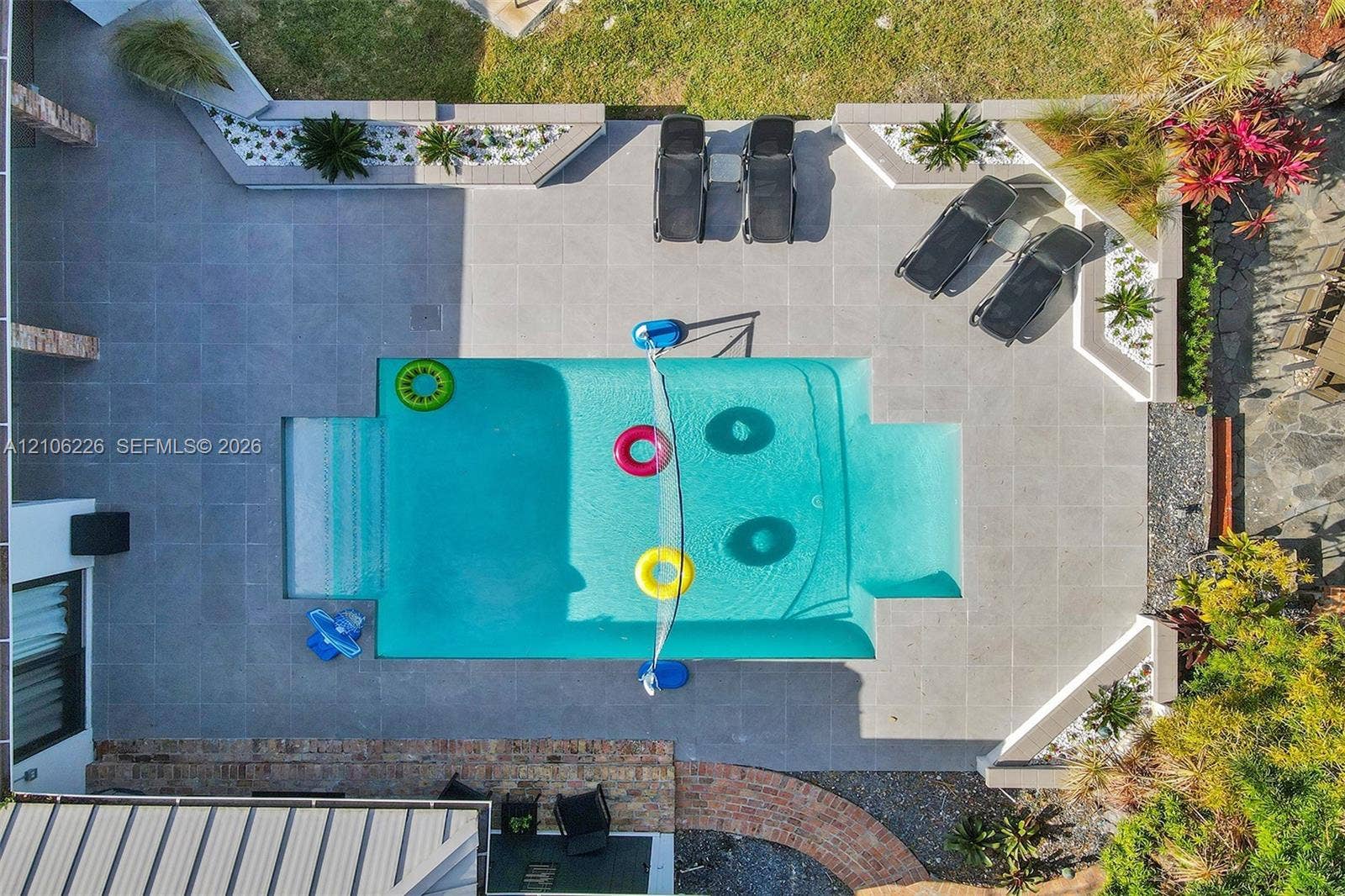 11155 SW 40th Street, Davie, FL 33328 Rectangular pool with integrated steps, surrounded by expansive gray tile decking, tiered concrete planter beds, and manicured landscaping