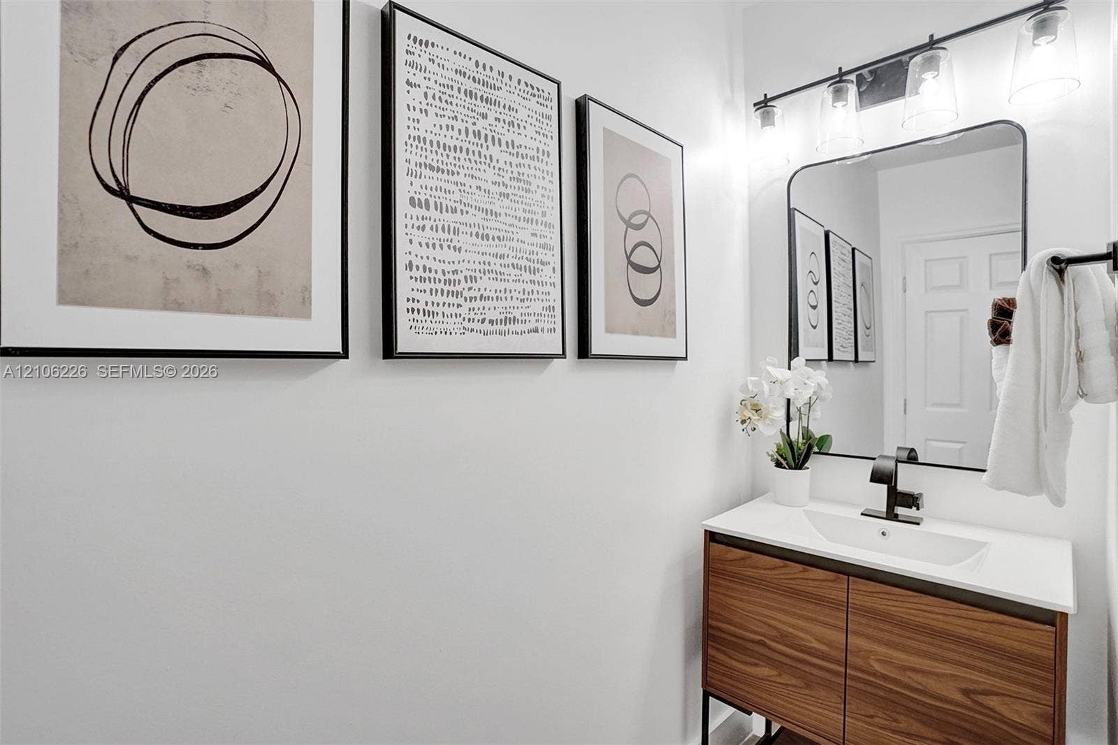 11155 SW 40th Street, Davie, FL 33328 Vanity with a wood-finish cabinet, integrated rectangular sink, matte black faucet, and a rectangular mirror with a matching black frame, illuminated by a multi-bulb light fixture