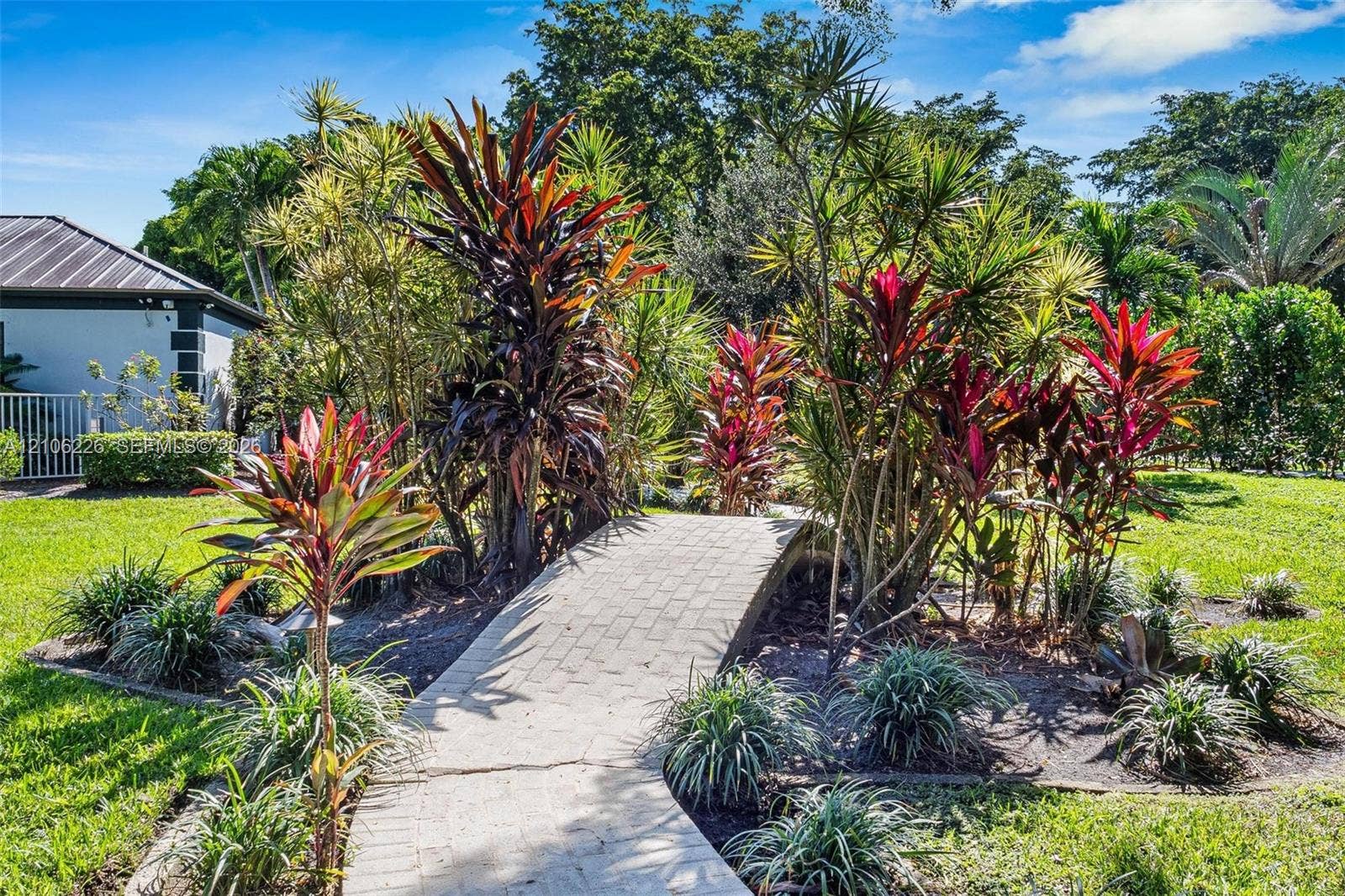 11155 SW 40th Street, Davie, FL 33328 Landscaped garden featuring a paved pedestrian bridge, mature tropical foliage, and expansive grass lawn