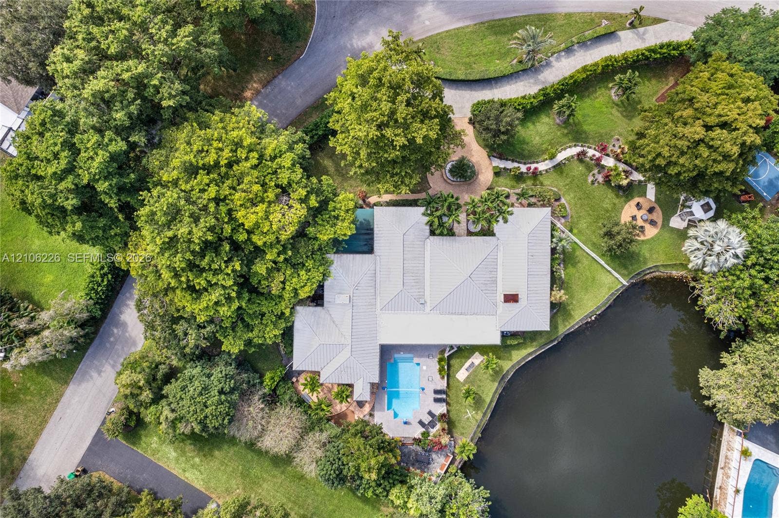 11155 SW 40th Street, Davie, FL 33328 Aerial perspective of a property featuring a swimming pool, waterfront location, extensive mature landscaping, paved walkway, and a multi-section roof structure