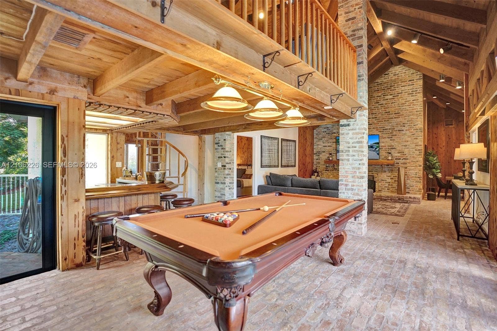 11155 SW 40th Street, Davie, FL 33328 Exposed timber beams and vaulted wood-paneled ceilings, floor-to-ceiling brick masonry fireplace, brick flooring, and custom spiral staircase with a wood-railed mezzanine