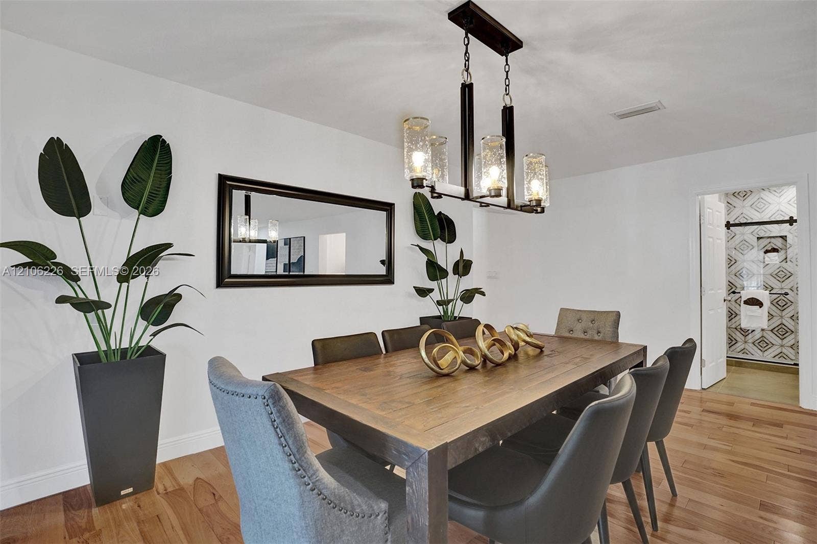 11155 SW 40th Street, Davie, FL 33328 Dining area featuring wood-finish flooring, a rectangular wall-mounted mirror with a dark frame, and a four-light linear chandelier with textured glass shades