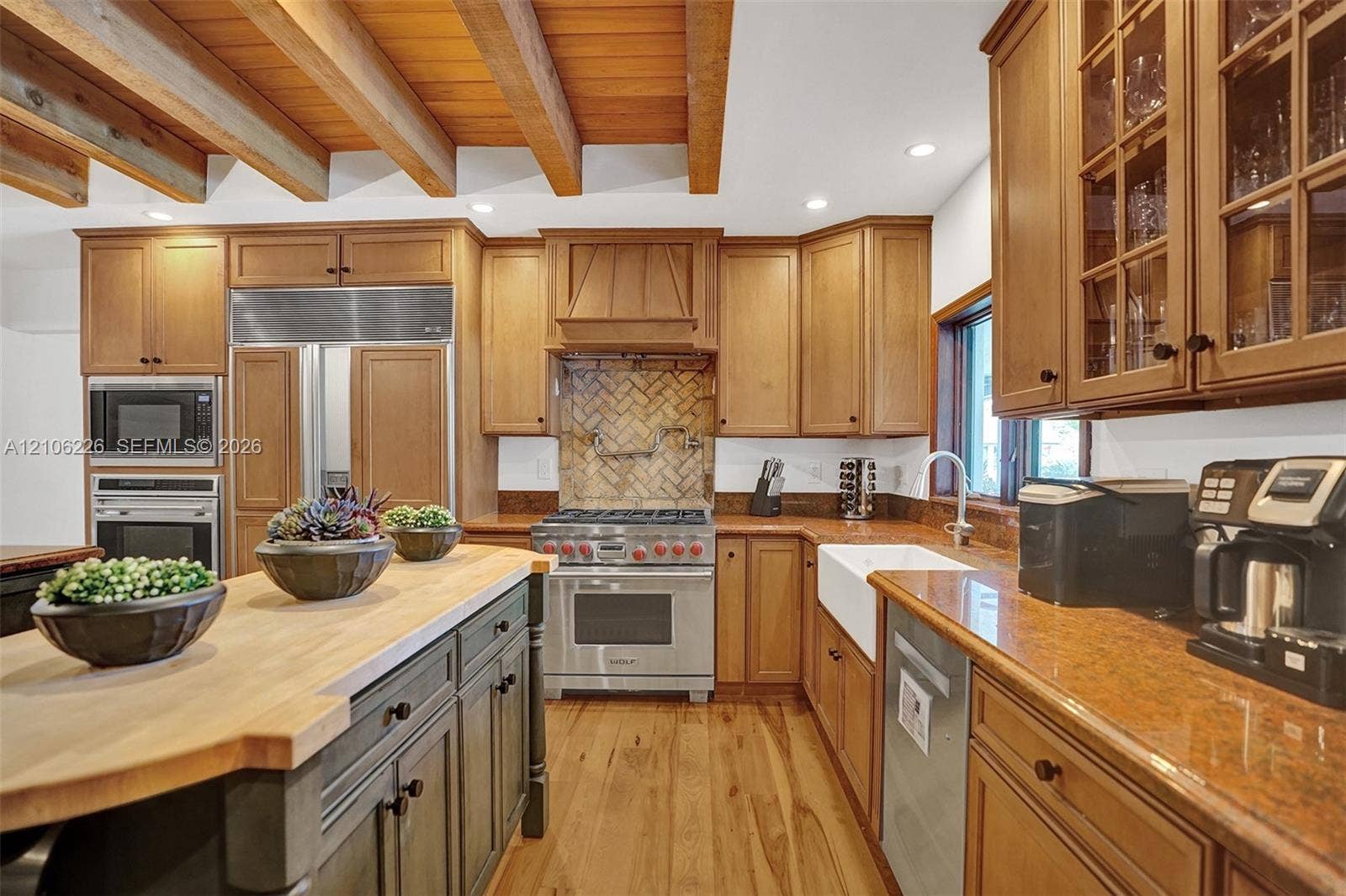 11155 SW 40th Street, Davie, FL 33328 Kitchen featuring exposed wood ceiling beams, wood-finish flooring, a butcher-block topped island, a farmhouse-style sink, and herringbone-patterned tile backsplash