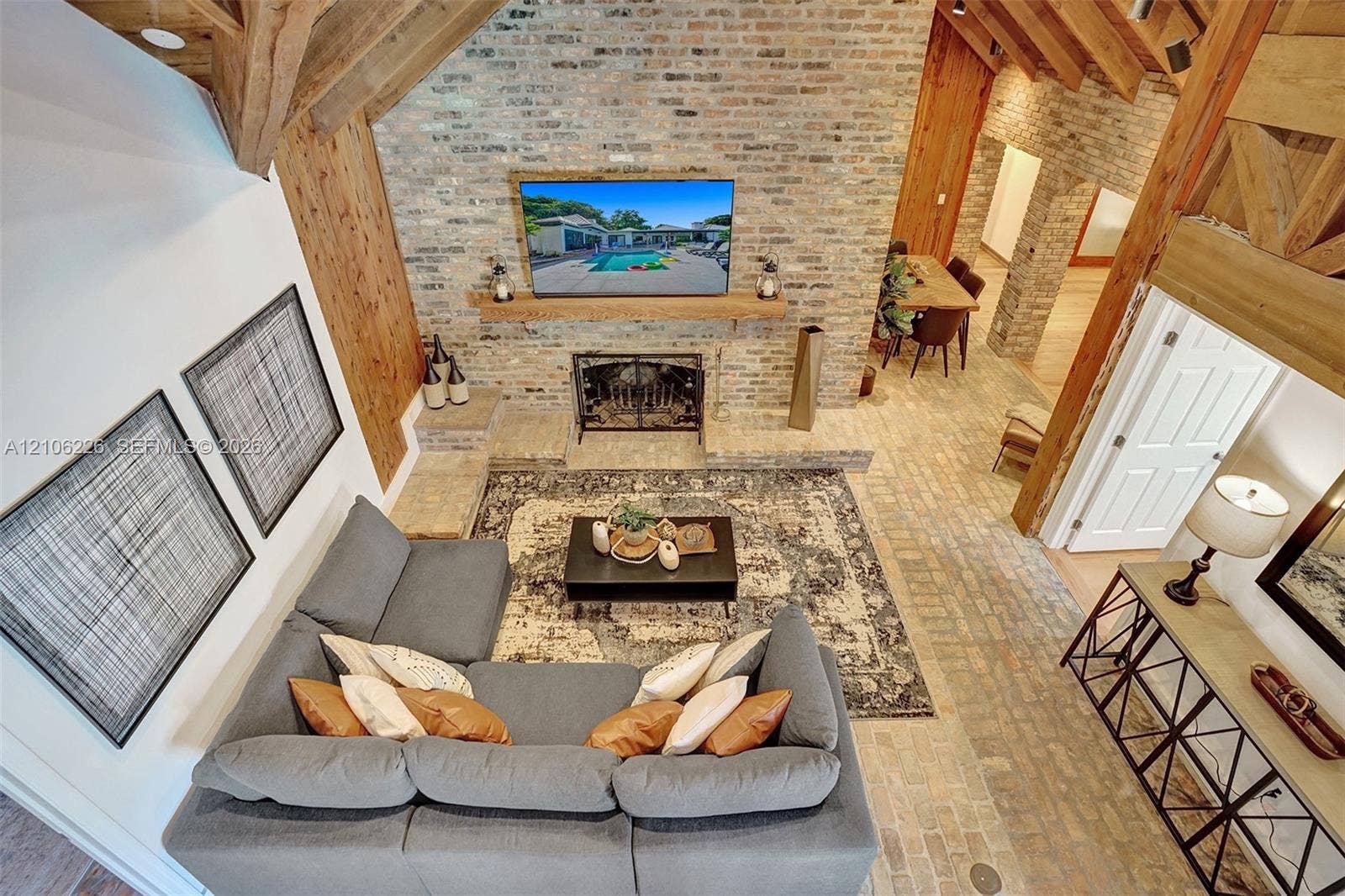 11155 SW 40th Street, Davie, FL 33328 Vaulted ceiling featuring exposed heavy timber beams, floor-to-ceiling reclaimed brick accent wall, wood-burning fireplace with brick hearth, and herringbone-patterned brick flooring