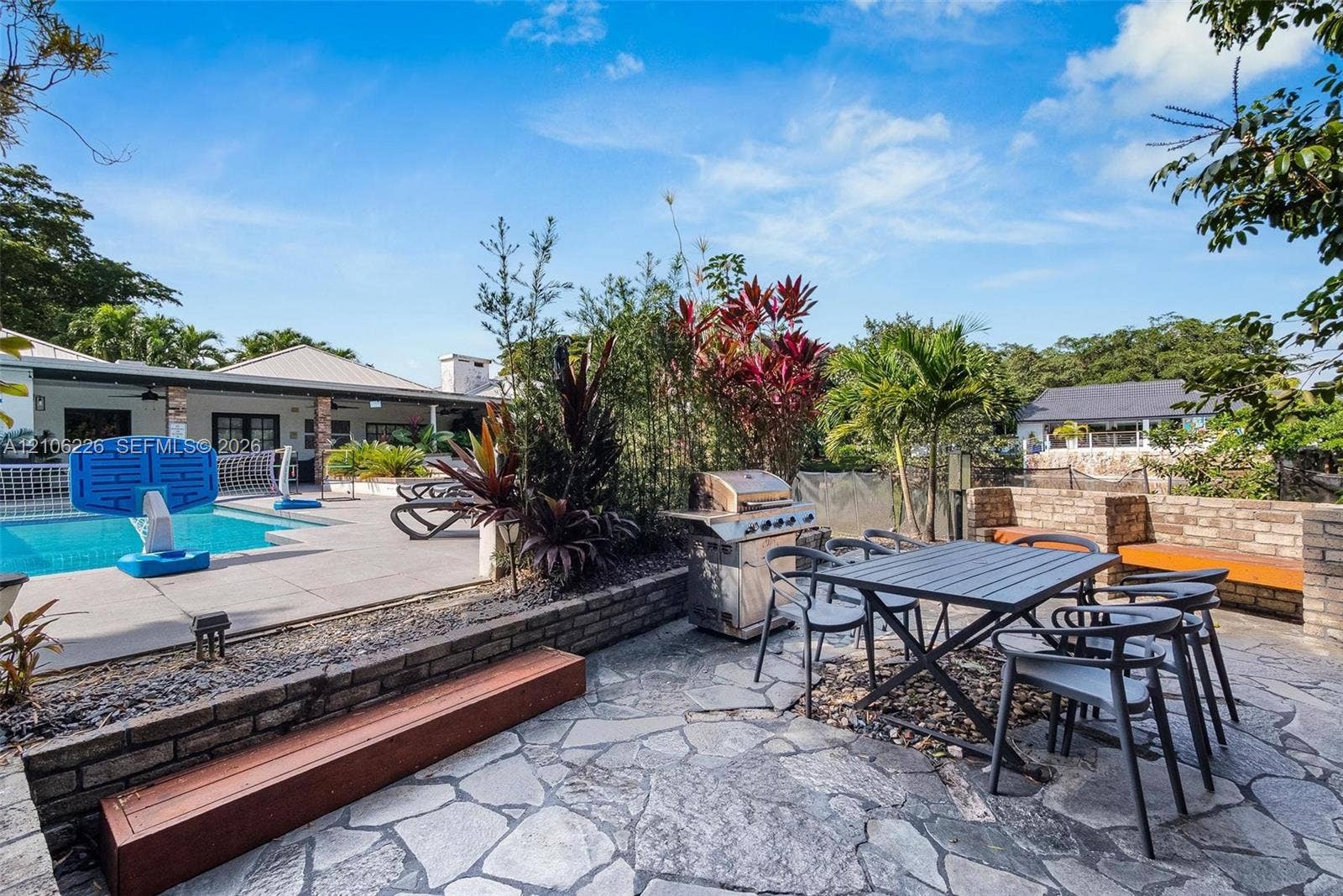 11155 SW 40th Street, Davie, FL 33328 Outdoor living area featuring a flagstone patio, built-in brick retaining walls, integrated bench seating, a permanent stainless-steel grill, and an inground swimming pool