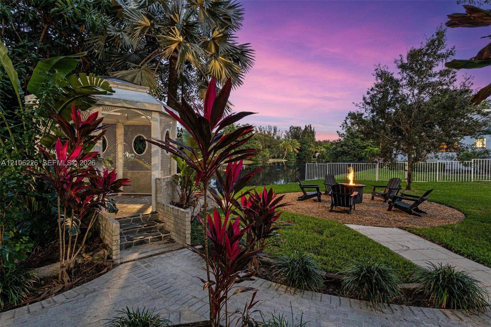 11155 SW 40th Street, Davie, FL 33328 Backyard featuring a custom gazebo with masonry steps, a circular stone-aggregate fire pit area, mature tropical landscaping, and water frontage
