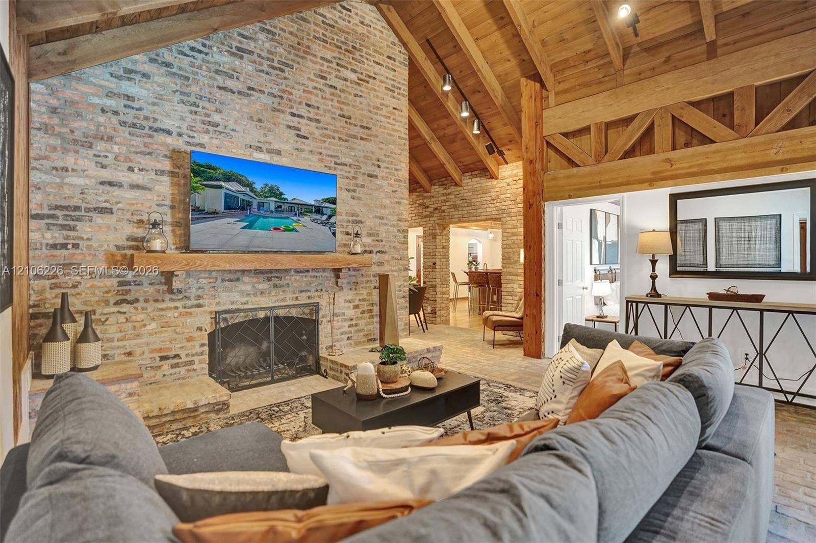 11155 SW 40th Street, Davie, FL 33328 Exposed brick fireplace with a wood mantel, vaulted wood-plank ceiling, and decorative timber truss detailing