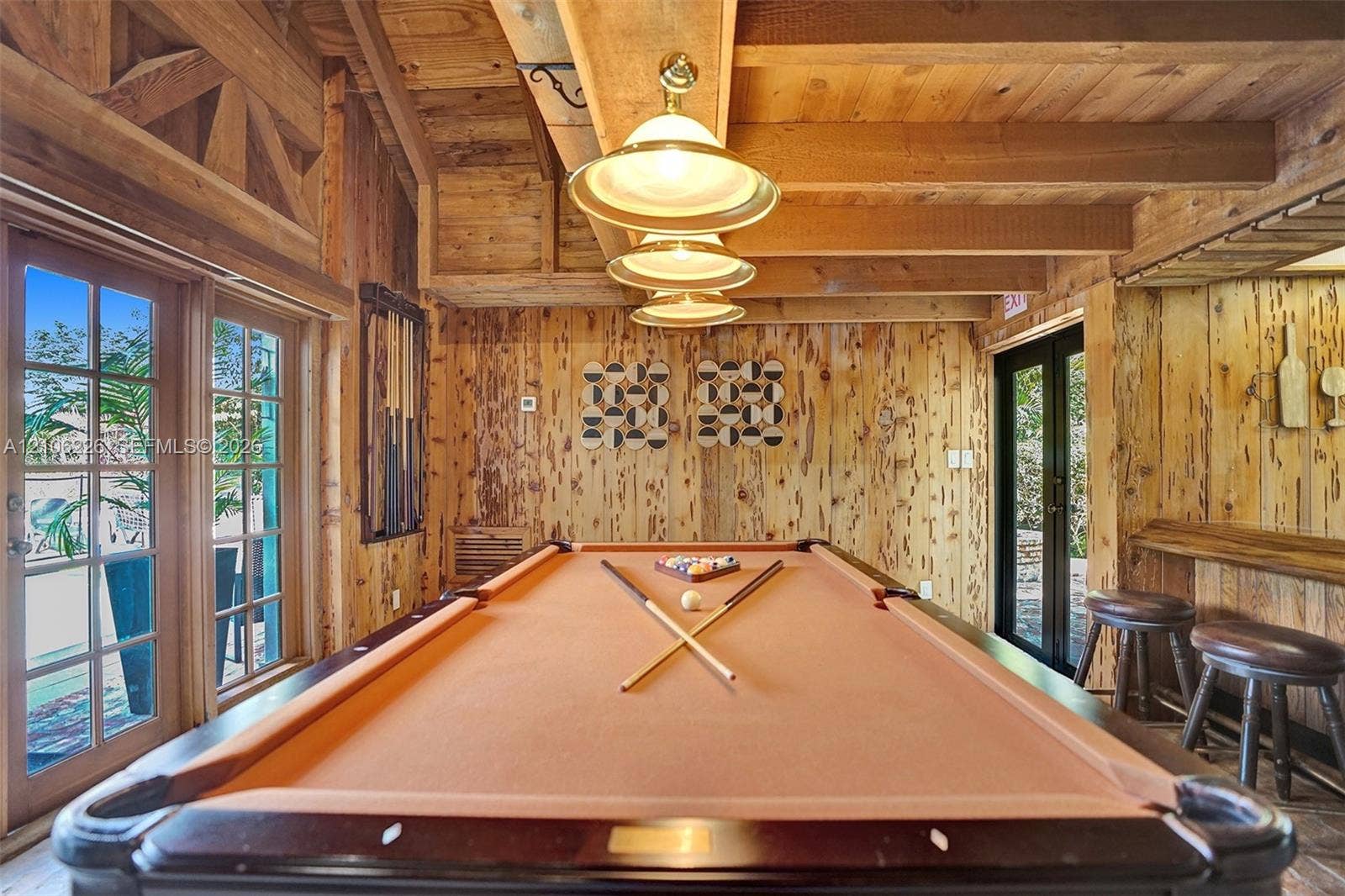 11155 SW 40th Street, Davie, FL 33328 Exposed timber ceiling beams, rustic wood wall paneling, dual sets of French doors, and multi-pendant brass lighting fixtures