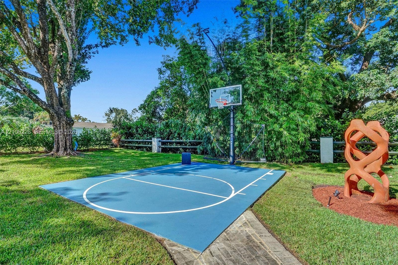 11155 SW 40th Street, Davie, FL 33328 Outdoor sports court with painted surface, basketball hoop, manicured lawn, and perimeter wood-post fencing