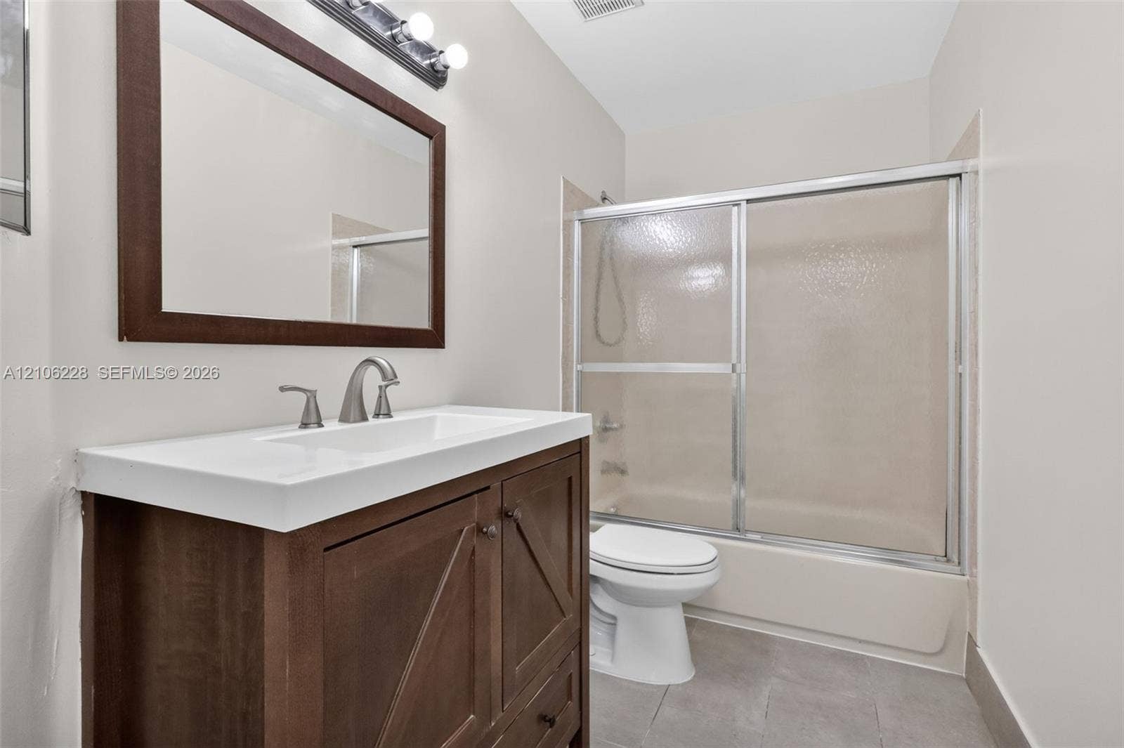 10760 SW 11th Drive, Davie, FL 33324 Bathroom featuring a dark wood-finish vanity with a white countertop, framed wall mirror, polished metal fixtures, and a shower-tub combination with sliding glass doors