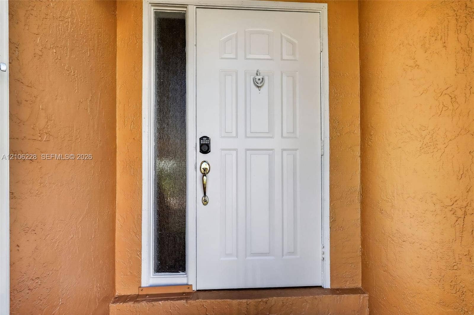 10760 SW 11th Drive, Davie, FL 33324 Entry door featuring a white six-panel design, textured stucco exterior wall, sidelight with privacy glass, metallic hardware, and door knocker