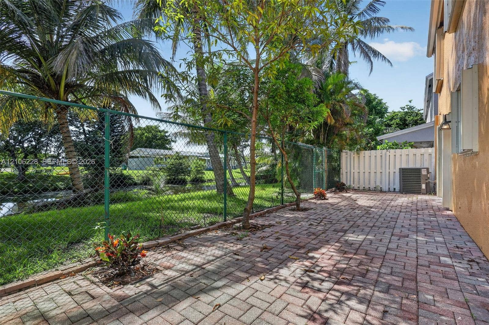 10760 SW 11th Drive, Davie, FL 33324 Rear patio featuring herringbone-patterned pavers, chain-link and privacy fencing, mature palm trees, and canal frontage