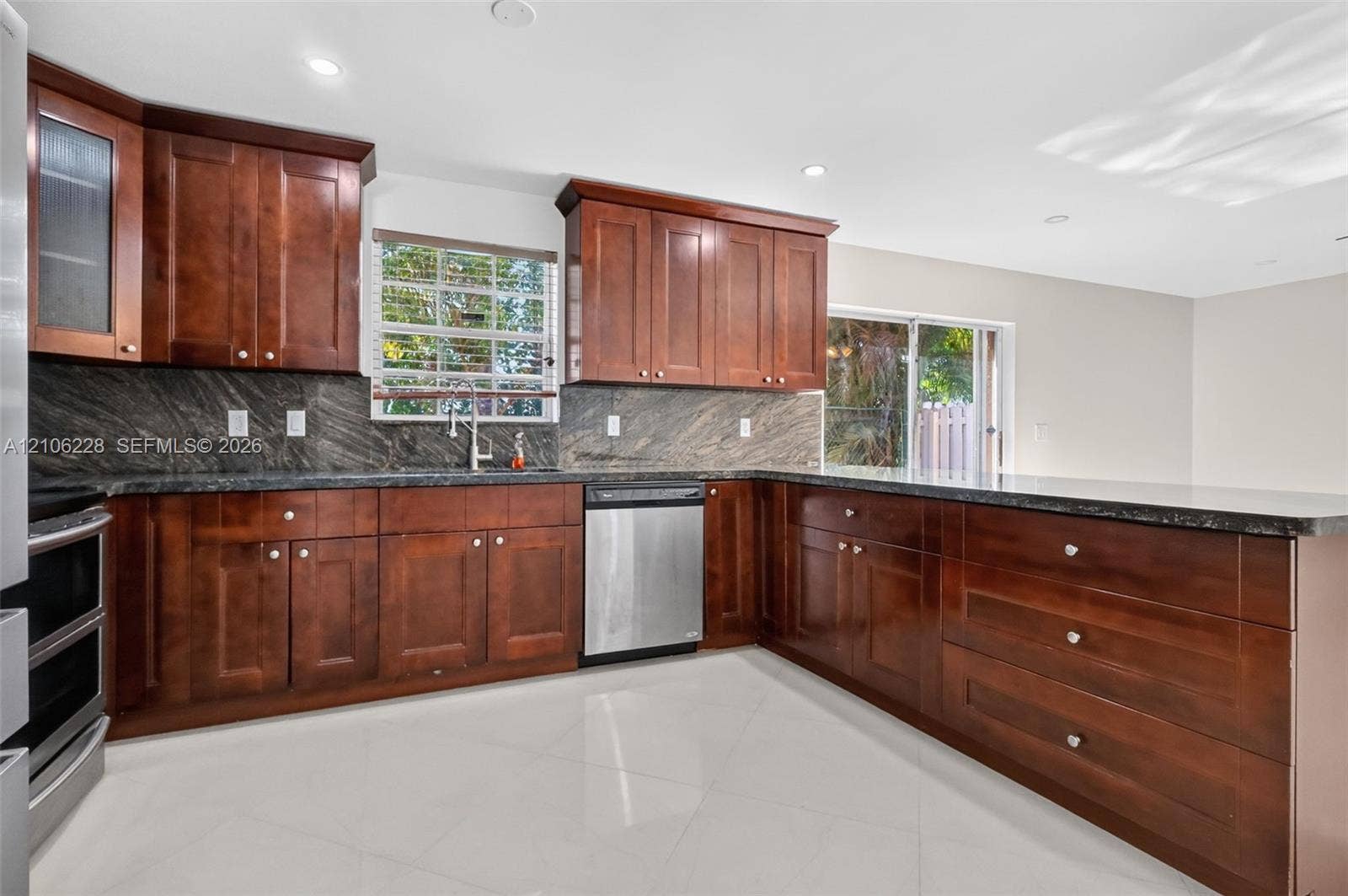 10760 SW 11th Drive, Davie, FL 33324 Kitchen featuring dark-toned wood cabinetry, stone countertops, stone backsplash, stainless steel dishwasher, and light-toned tile flooring
