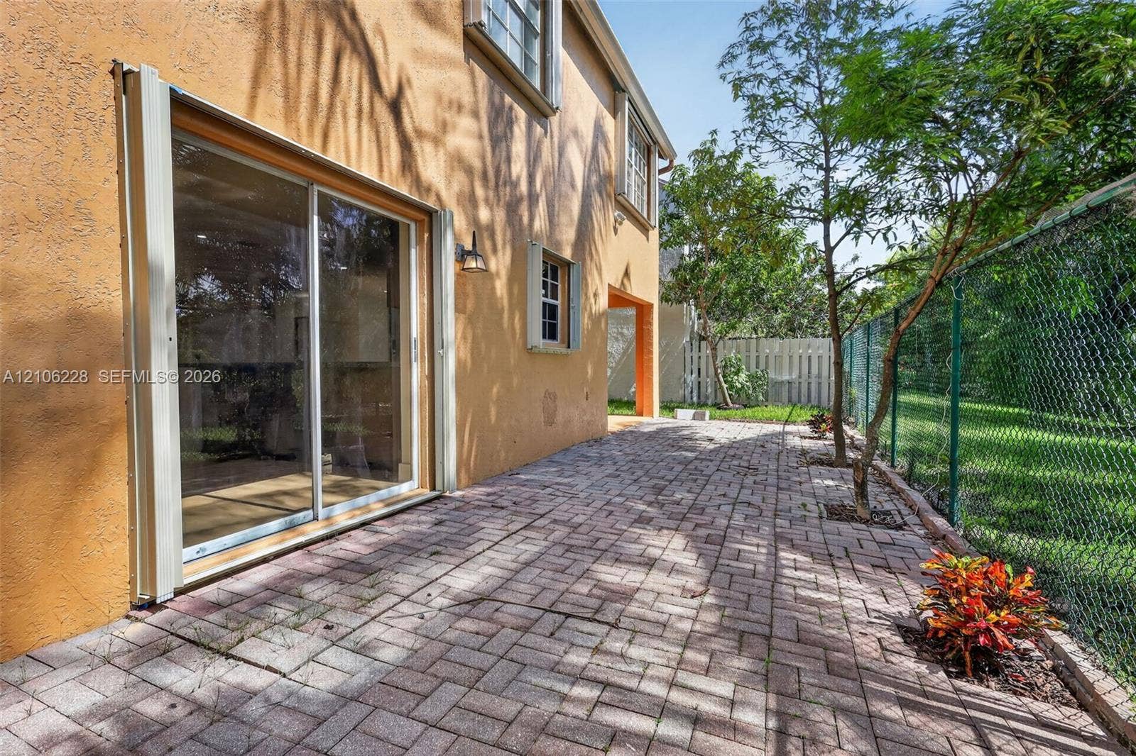 10760 SW 11th Drive, Davie, FL 33324 Stucco exterior featuring a paver patio, sliding glass door, and chain-link perimeter fencing