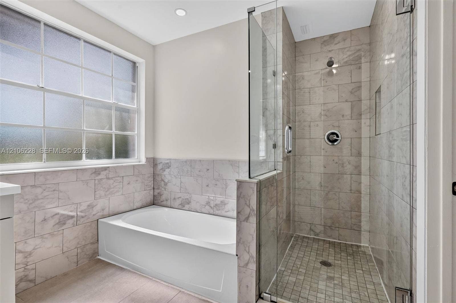 10760 SW 11th Drive, Davie, FL 33324 Bathroom featuring a deep soaking tub, separate glass-enclosed shower with a recessed niche, stone-patterned wall tile, frosted window, and brushed-nickel hardware