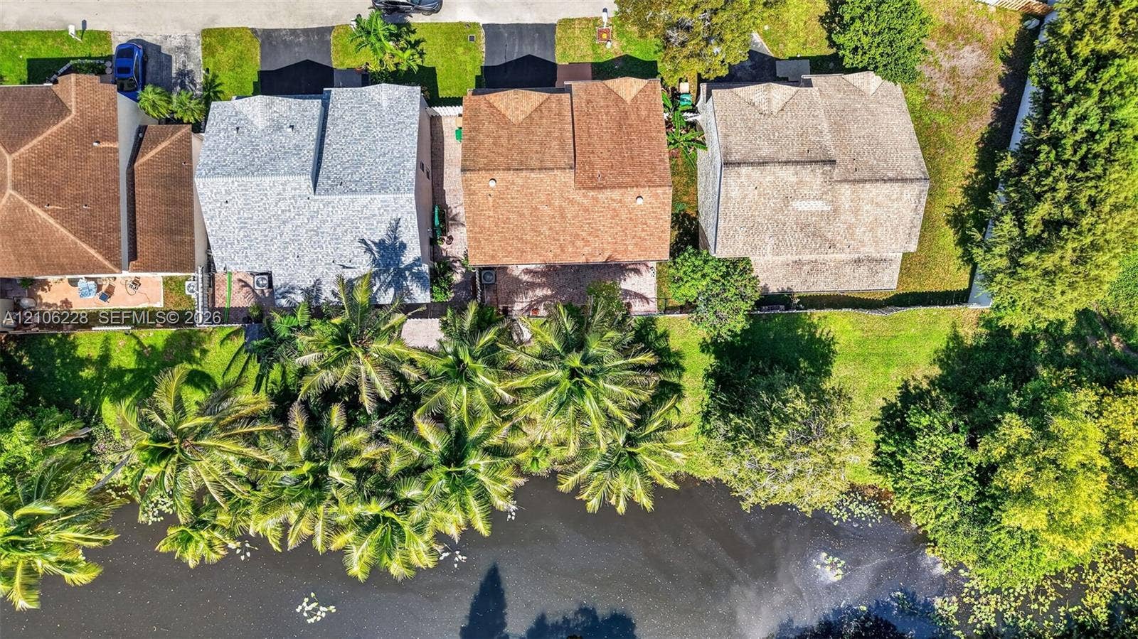 10760 SW 11th Drive, Davie, FL 33324 Aerial perspective featuring waterfront property with mature palm trees, paved rear patios, asphalt driveways, and shingled rooflines