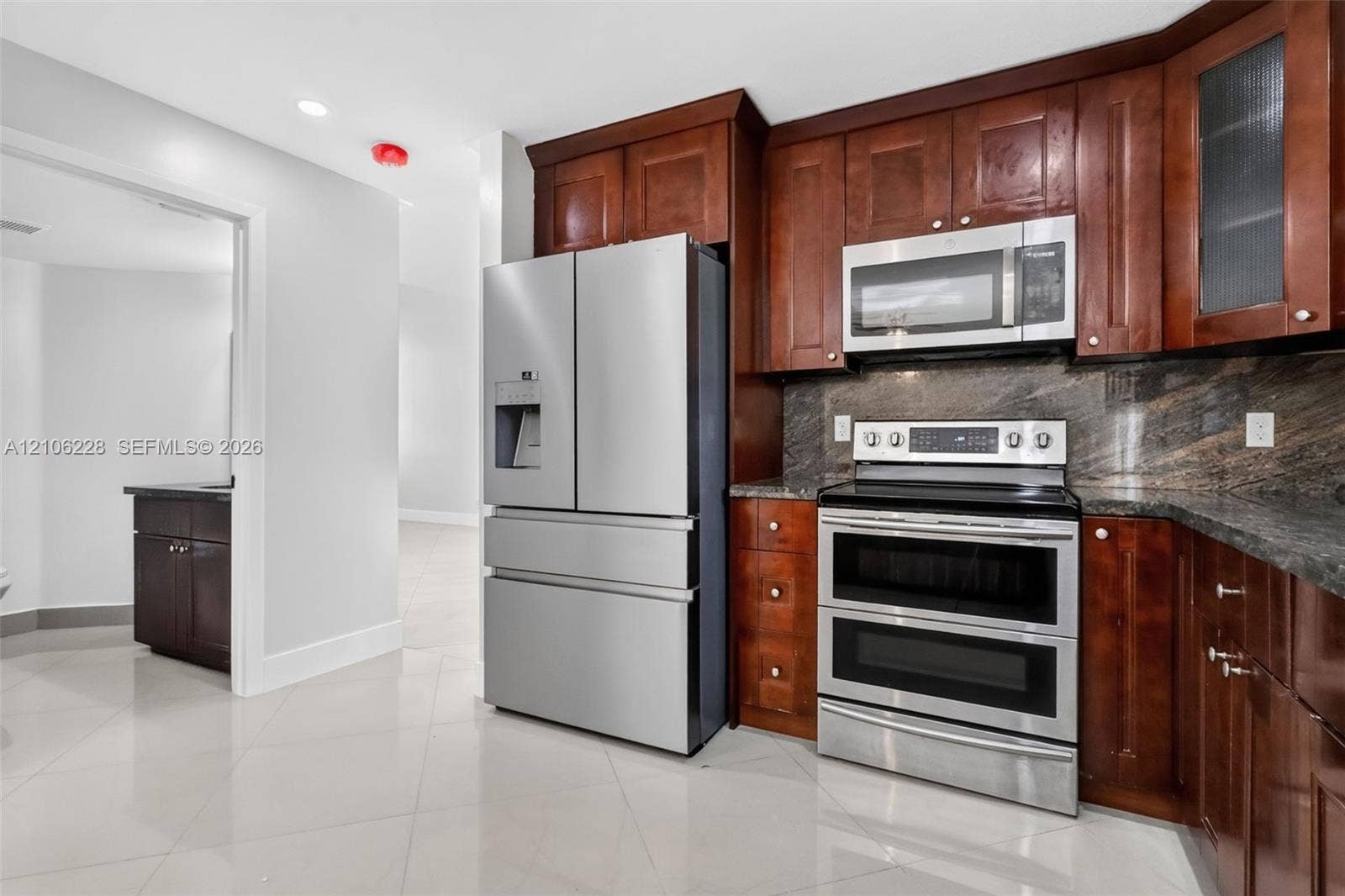 10760 SW 11th Drive, Davie, FL 33324 Kitchen featuring dark wood-finish cabinetry, stone backsplash, stainless steel appliances, and large-format tile flooring