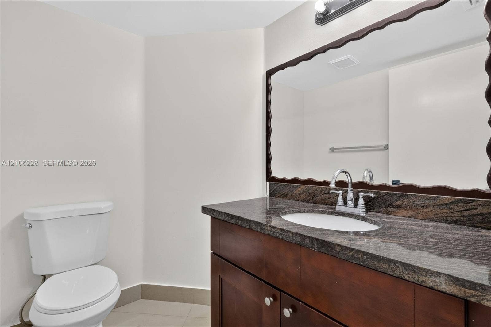 10760 SW 11th Drive, Davie, FL 33324 Dark wood-finish cabinetry with a stone-top vanity, undermount sink, dual-handle faucet, and decorative-edge wall mirror