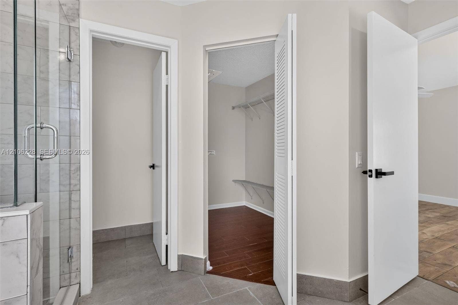 10760 SW 11th Drive, Davie, FL 33324 Glass-enclosed shower with tiled surround, walk-in closet featuring wire shelving, wood-finish flooring, and minimalist doors with matte black hardware