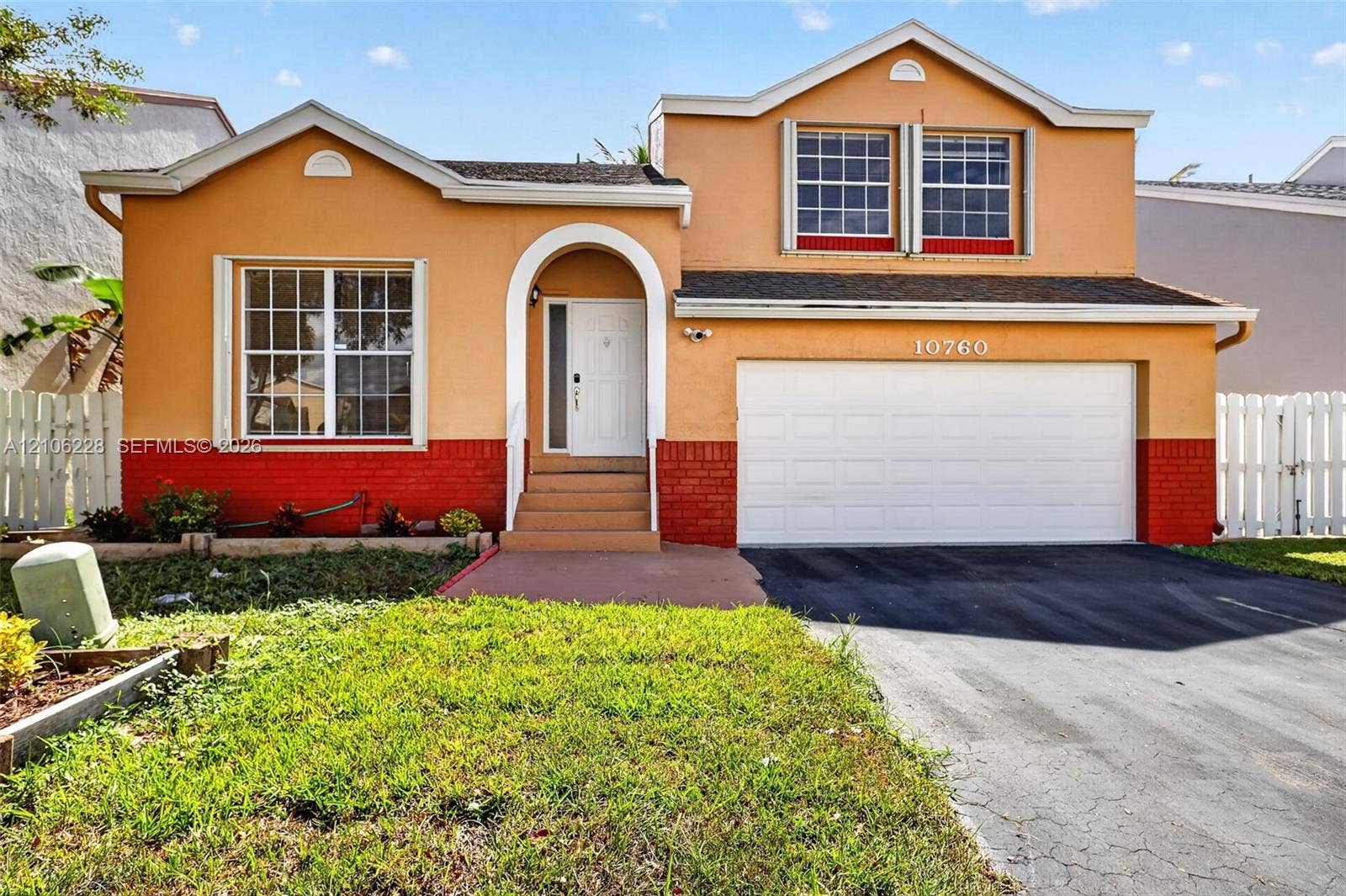 10760 SW 11th Drive, Davie, FL 33324 Two-story residence featuring a stucco and brick facade, an arched entry, a multi-pane window configuration, and an attached two-car garage