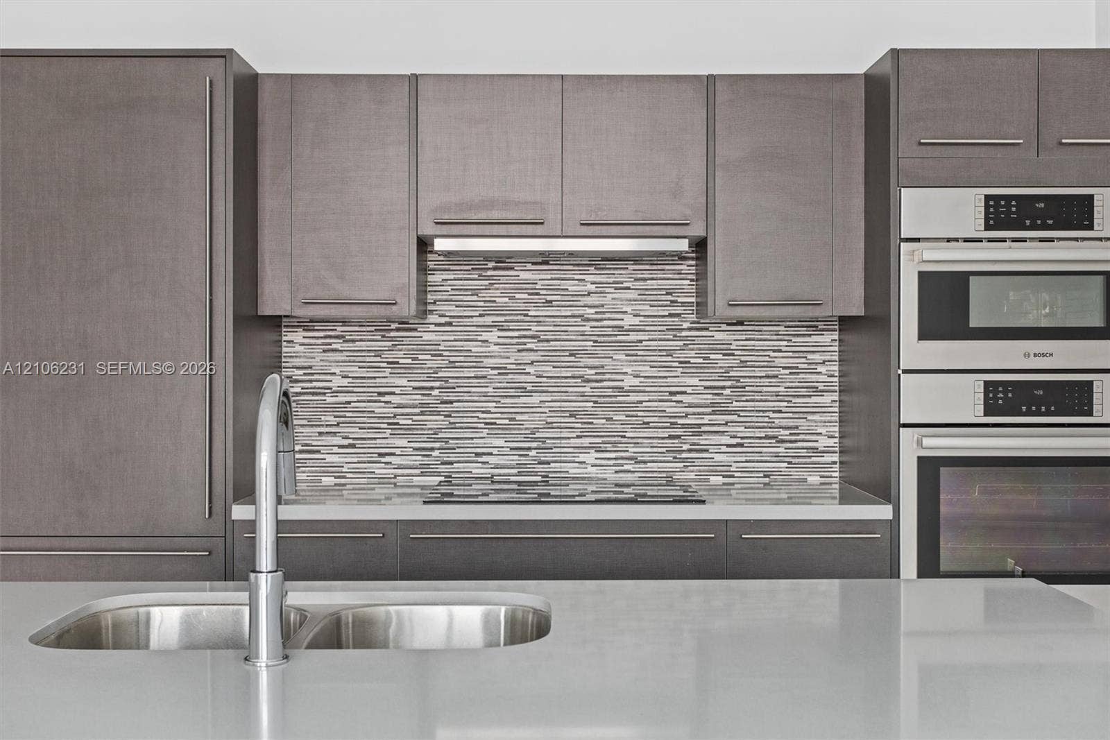 7875 NW 107th Avenue, #802, Doral, FL 33178 Modern kitchen featuring flat-panel cabinetry, quartz countertops, a mosaic tile backsplash, integrated stainless steel appliances, and a double-basin undermount sink with a gooseneck faucet
