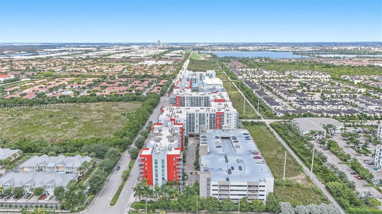 7875 NW 107th Avenue, #802, Doral, FL 33178 Aerial perspective featuring multi-story residential buildings with red and gray accents, integrated multi-level parking structure, and landscaped ground-level palms