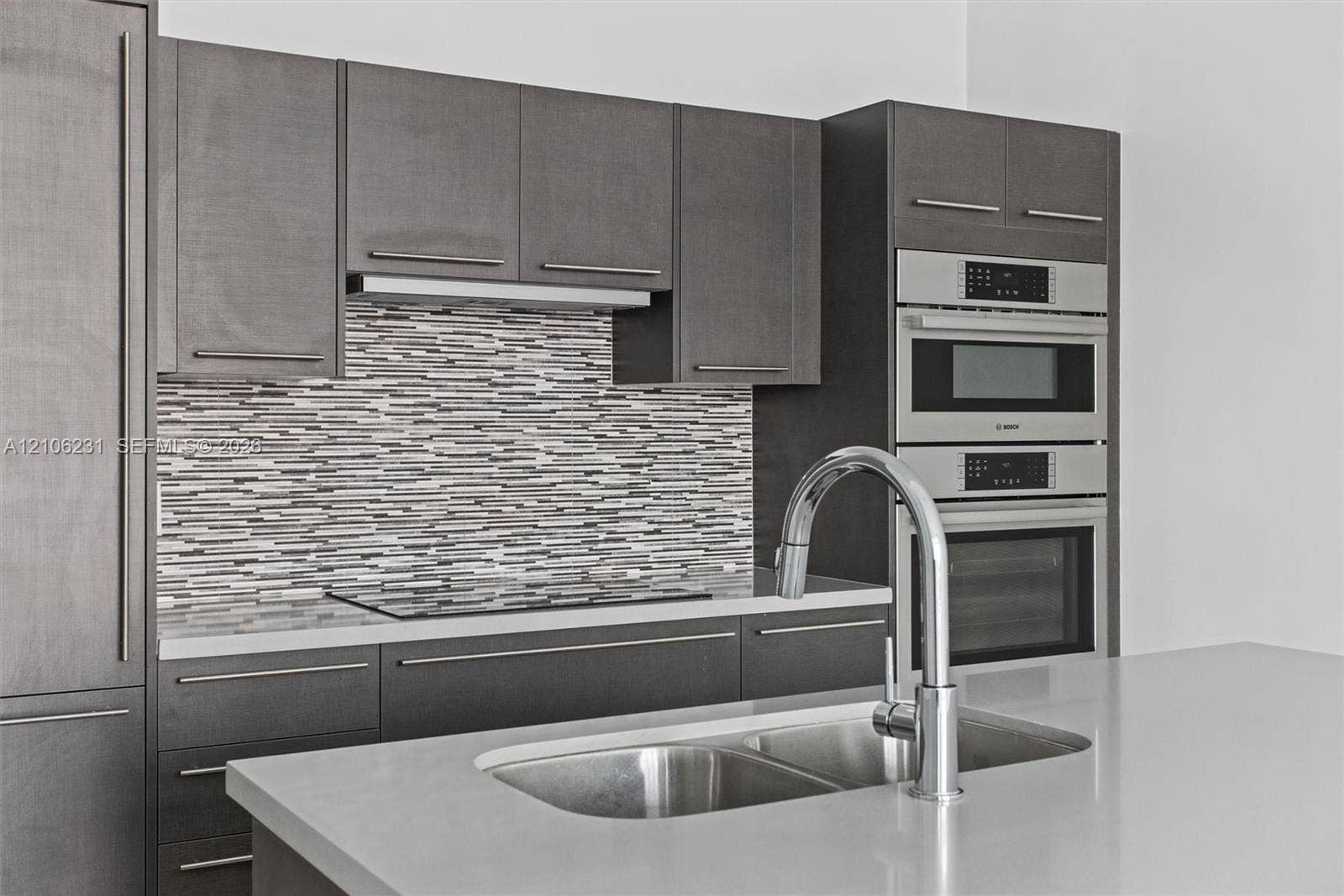 7875 NW 107th Avenue, #802, Doral, FL 33178 Flat-panel cabinetry, stacked stone tile backsplash, stone countertop, stainless steel double-basin sink with pull-down faucet, and built-in Bosch stainless steel double oven