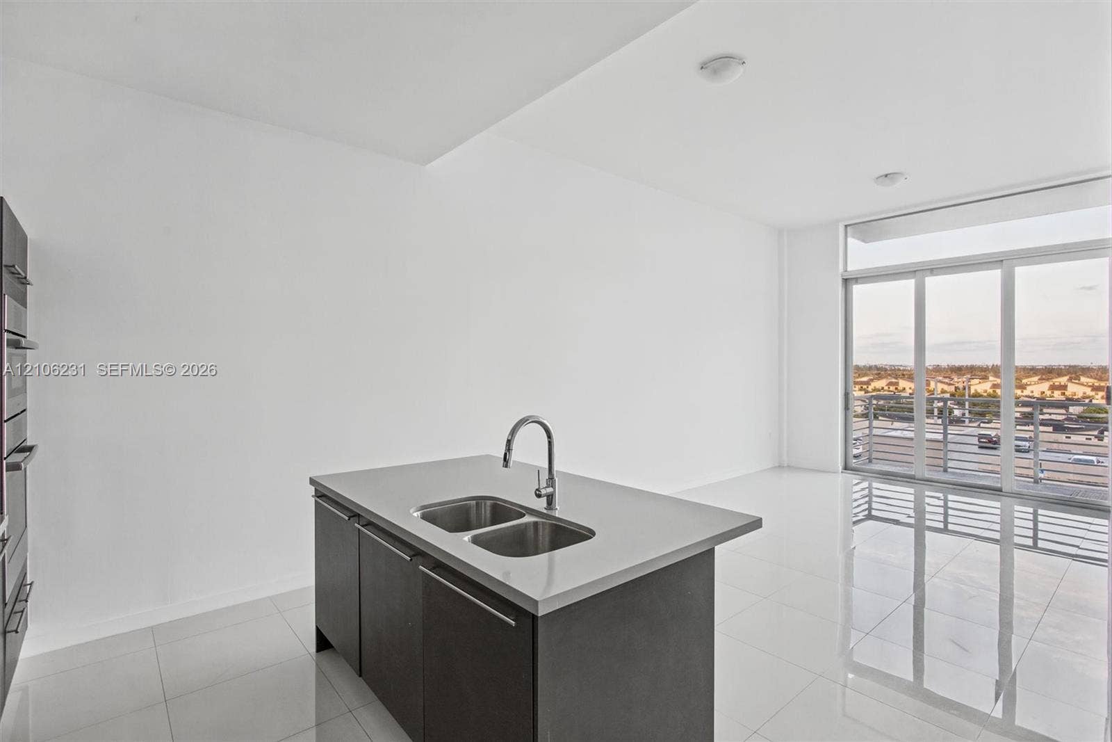 7875 NW 107th Avenue, #802, Doral, FL 33178 Kitchen island featuring a dual-basin stainless steel sink, solid surface countertop, and dark-toned cabinetry.