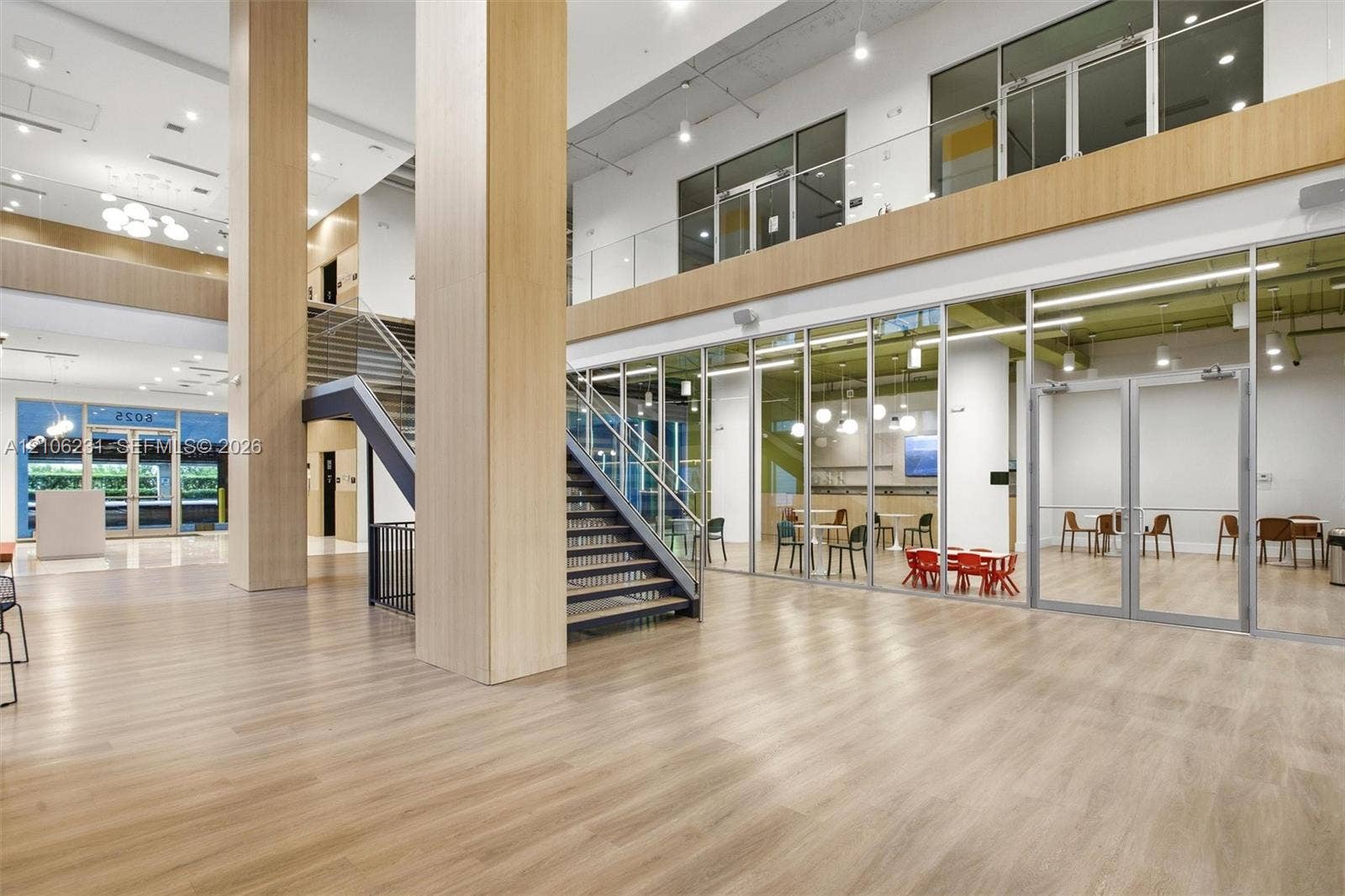 7875 NW 107th Avenue, #802, Doral, FL 33178 Atrium featuring a double-height ceiling, wood-finish flooring, floor-to-ceiling glass partitions, a prominent central staircase with metal railings, and dual-level mezzanine construction