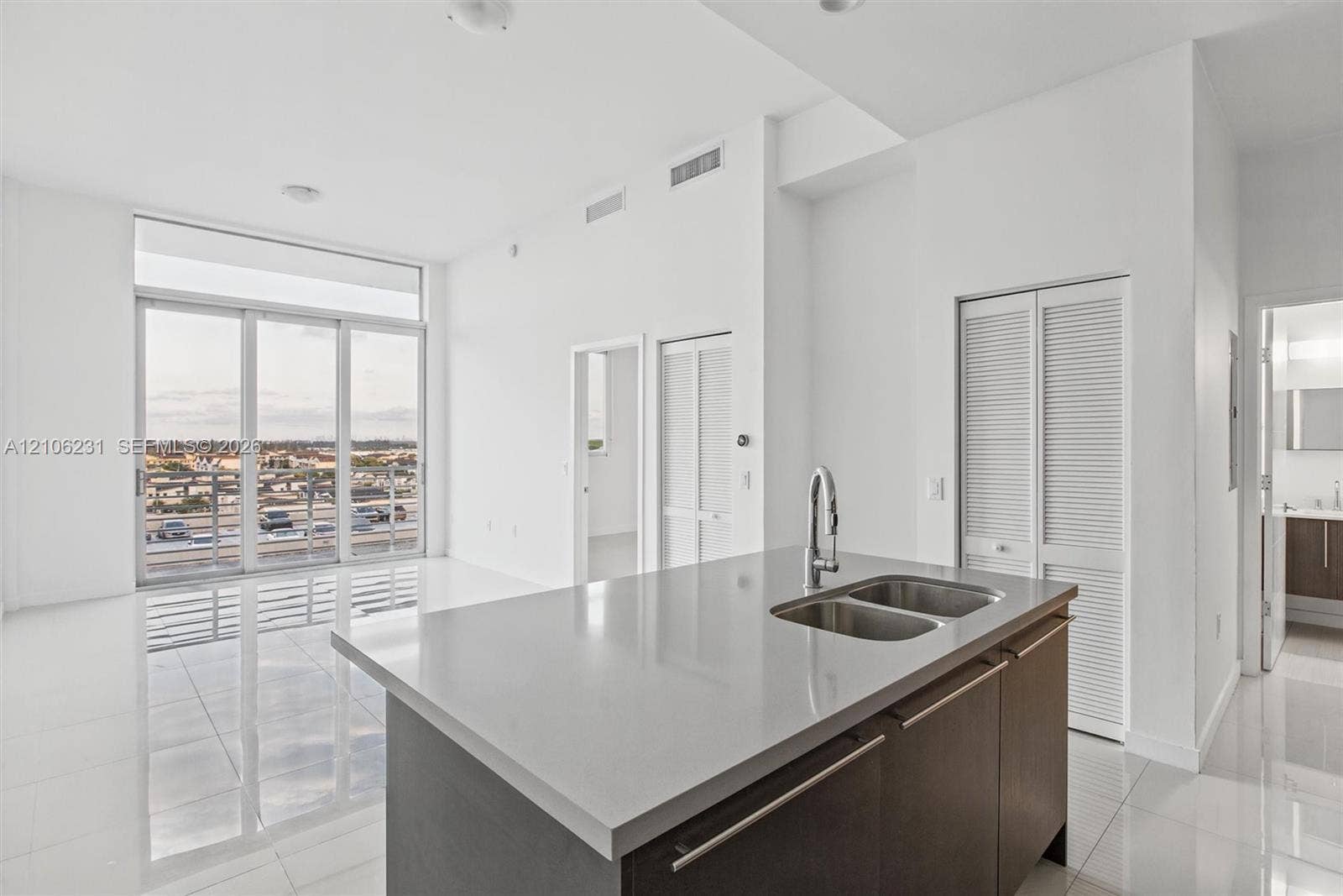 7875 NW 107th Avenue, #802, Doral, FL 33178 Open-concept kitchen featuring an island with a stone-composite countertop, dual-basin stainless steel sink, and high-arc faucet, complemented by floor-to-ceiling windows and polished tile flooring