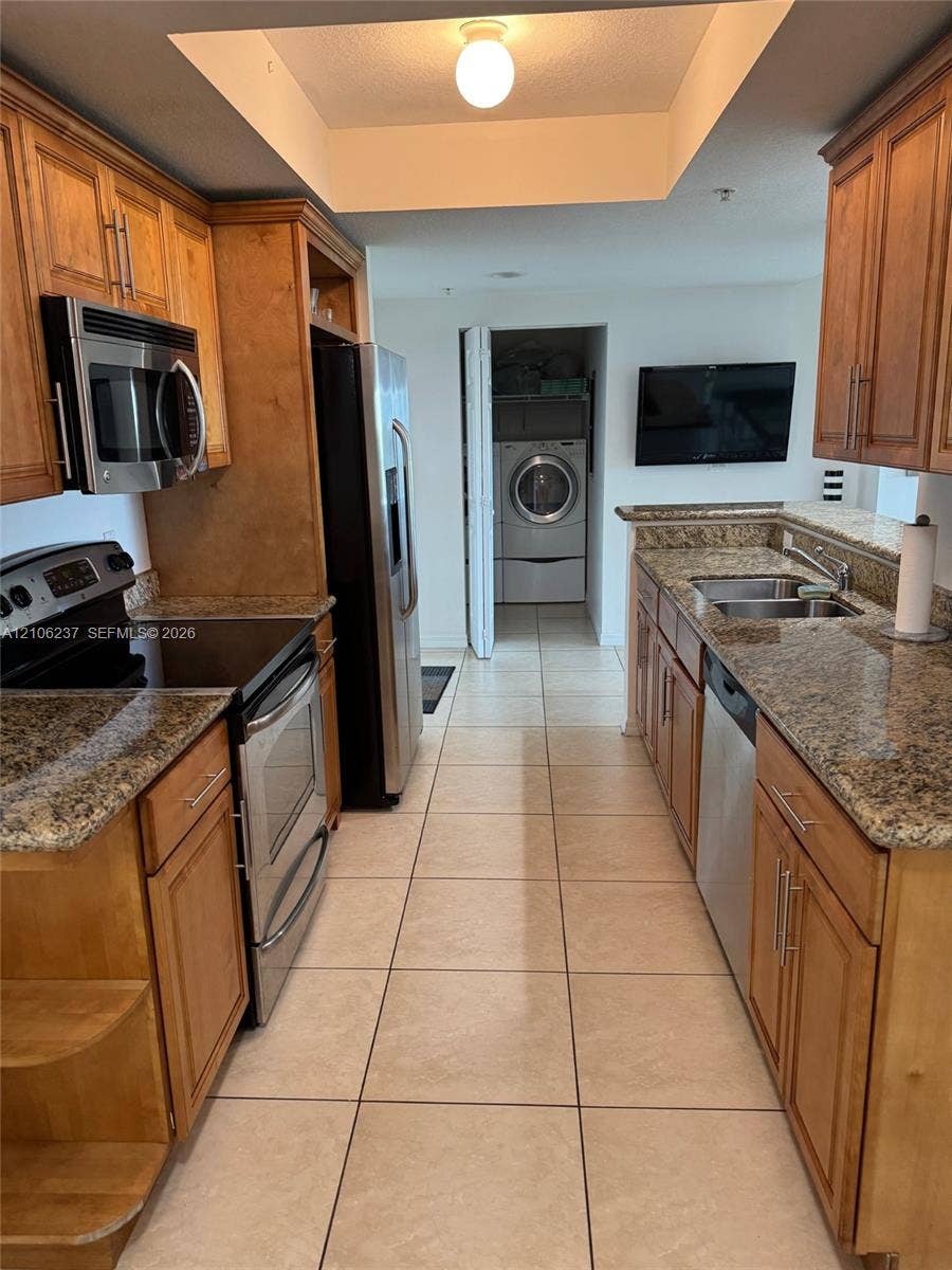3530 SW 22nd Street, #706, Miami, Miami, FL 33145 Kitchen featuring natural-finish wood cabinetry, stone countertops, stainless steel appliances, ceramic tile flooring, and an integrated laundry closet