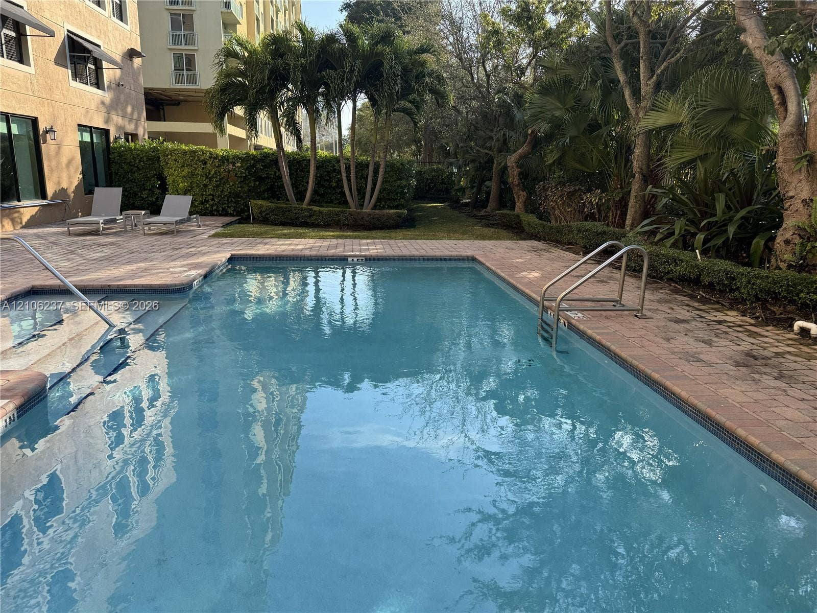 3530 SW 22nd Street, #706, Miami, Miami, FL 33145 Swimming pool featuring paver decking, metal handrails, integrated steps, and mature landscaping