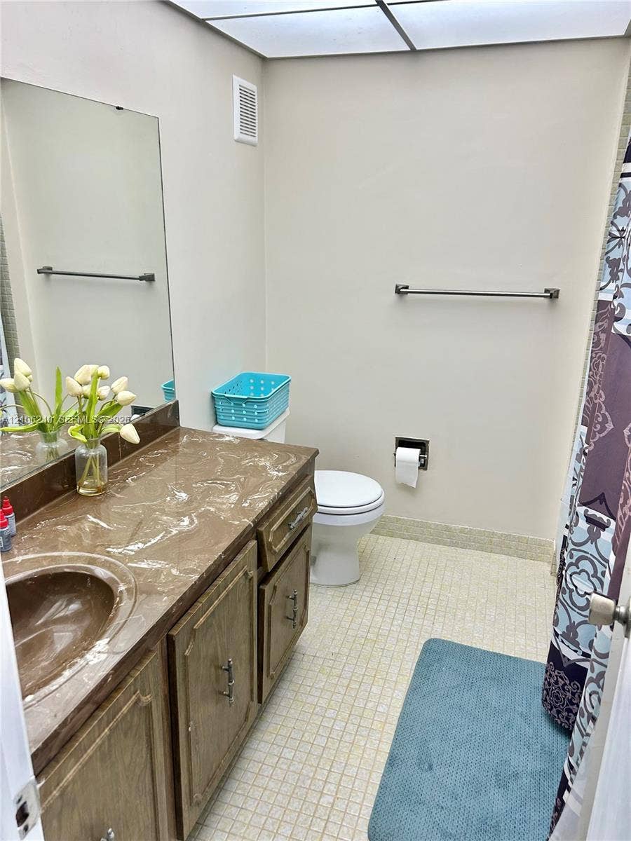 2554 N 38th Avenue, Hollywood, FL 33021 Bathroom featuring a wood-tone vanity with a molded countertop and integrated sink, large wall-mounted mirror, grid-patterned tile flooring, and a recessed ceiling lighting panel