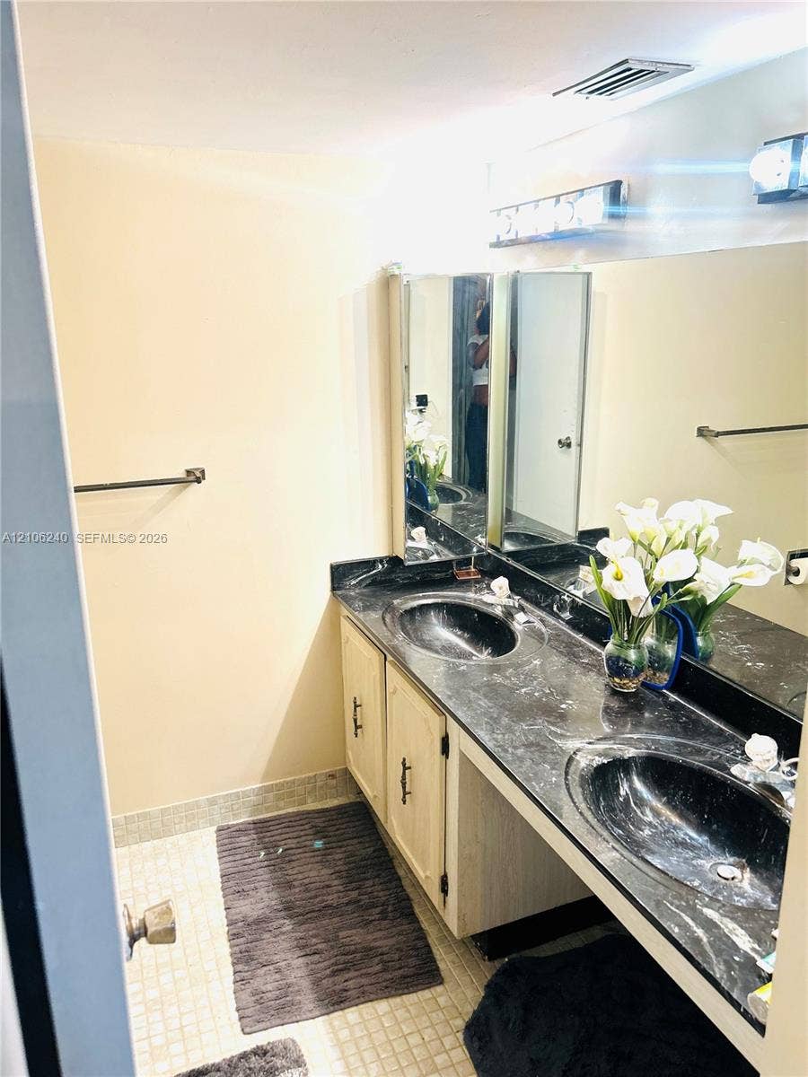 2554 N 38th Avenue, Hollywood, FL 33021 Extended vanity featuring dual oval undermount sinks, a dark stone countertop, light-toned cabinetry with metal hardware, and a full-width wall-mounted mirror