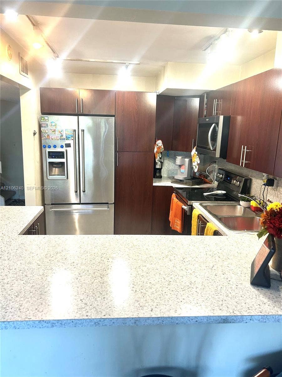 2554 N 38th Avenue, Hollywood, FL 33021 Kitchen featuring dark wood-finish cabinetry, stainless steel appliances, speckled stone-composite countertops, a dual-basin stainless steel sink, and track lighting