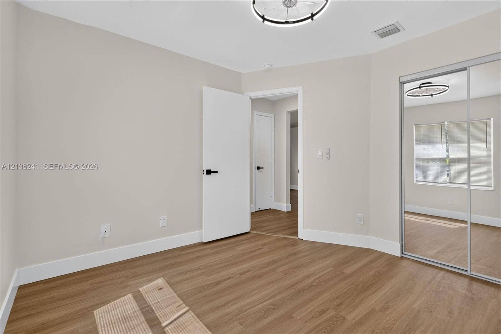 9407 SW 18th Street, Miramar, FL 33025 Neutral-toned interior featuring wood-finish flooring, sliding mirror-panel closet doors, and modern circular flush-mount lighting with matte black hardware