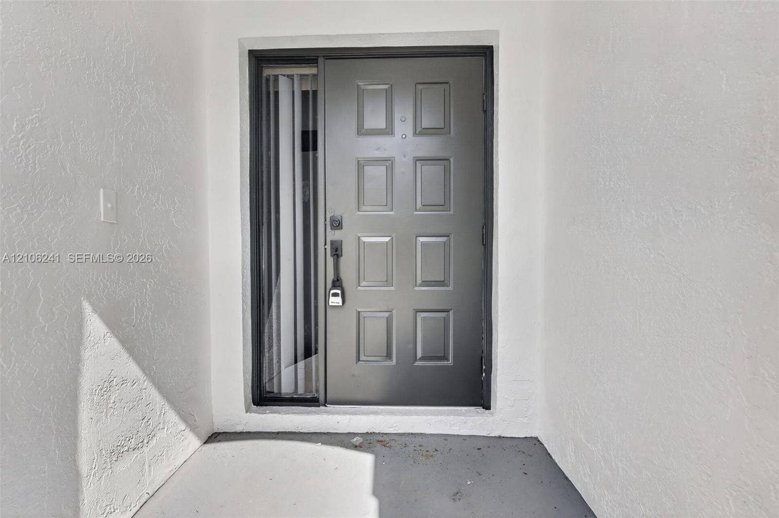 9407 SW 18th Street, Miramar, FL 33025 Grey paneled entry door with integrated vertical sidelight, framed by white textured exterior wall surfaces