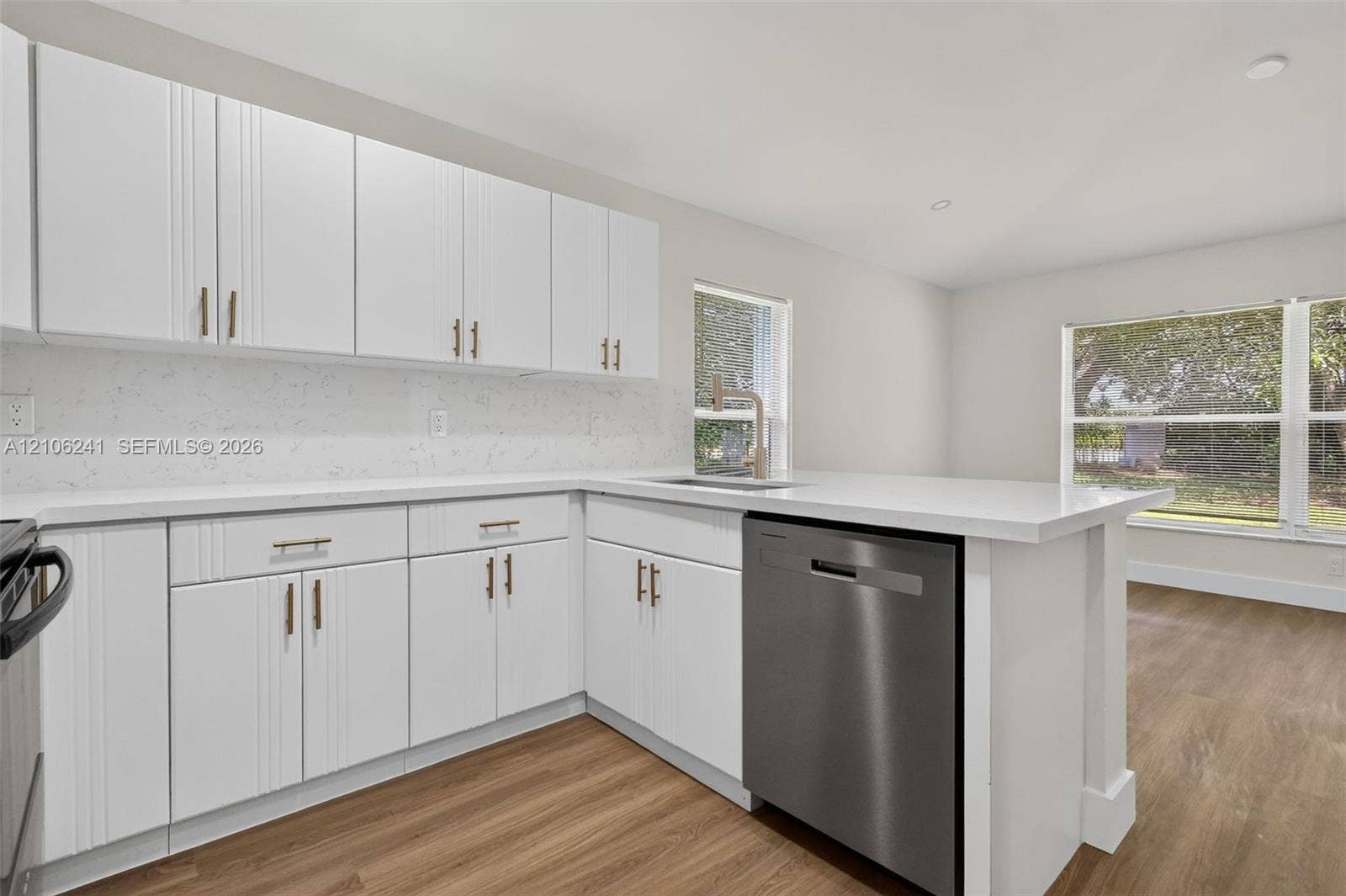 9407 SW 18th Street, Miramar, FL 33025 Kitchen featuring white shaker-style cabinetry, quartz countertops with matching backsplash, wood-finish flooring, stainless steel dishwasher, and metallic hardware