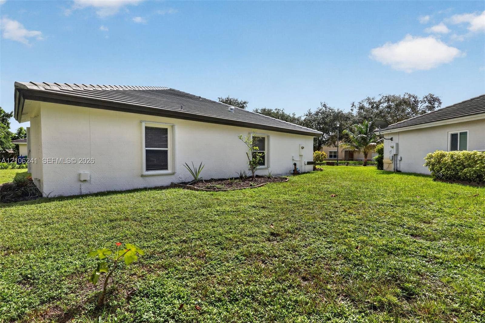 9407 SW 18th Street, Miramar, FL 33025 Exterior elevation featuring light-colored stucco siding, a low-pitch roof, inset single-hung windows, and a grass-covered backyard