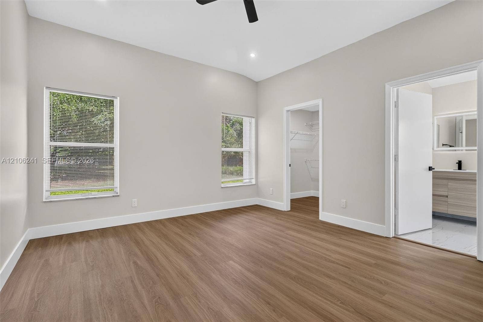 9407 SW 18th Street, Miramar, FL 33025 Room featuring neutral wall paint, wood-finish flooring, two windows, a walk-in closet with built-in wire shelving, and a black ceiling fan