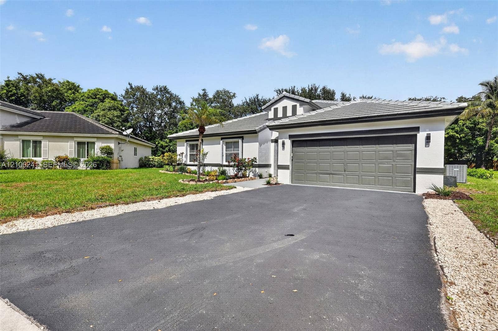 9407 SW 18th Street, Miramar, FL 33025 Single-story exterior featuring a multi-gabled roofline, light-toned stucco facade, multi-panel garage door, and a paved driveway lined with stone accents