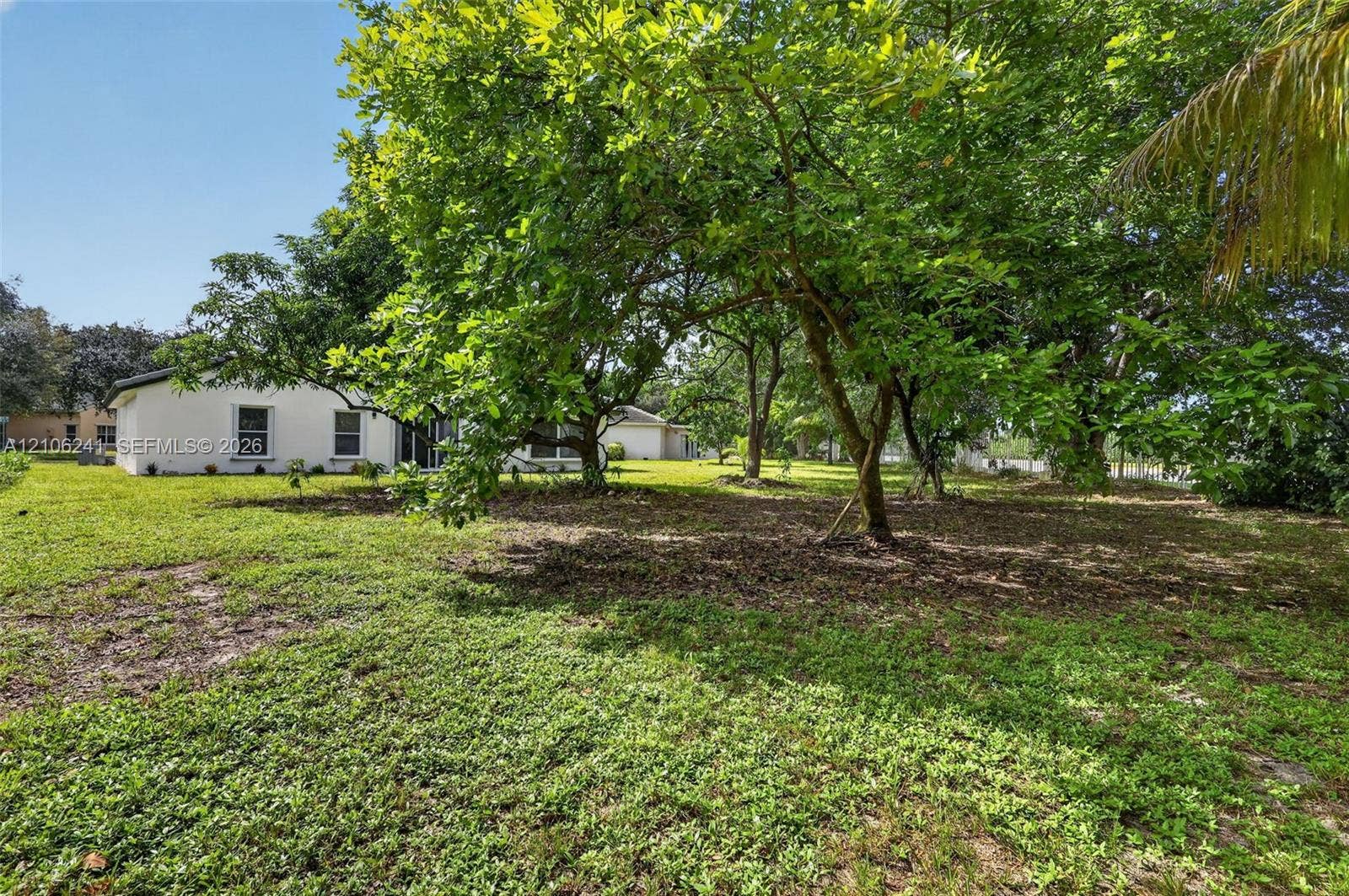 9407 SW 18th Street, Miramar, FL 33025 Expansive backyard featuring mature shade trees, a manicured lawn, and a stucco exterior residence