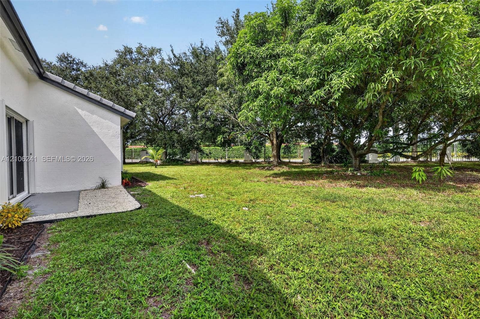 9407 SW 18th Street, Miramar, FL 33025 Exterior yard featuring mature trees, stucco siding, and a paved concrete patio area